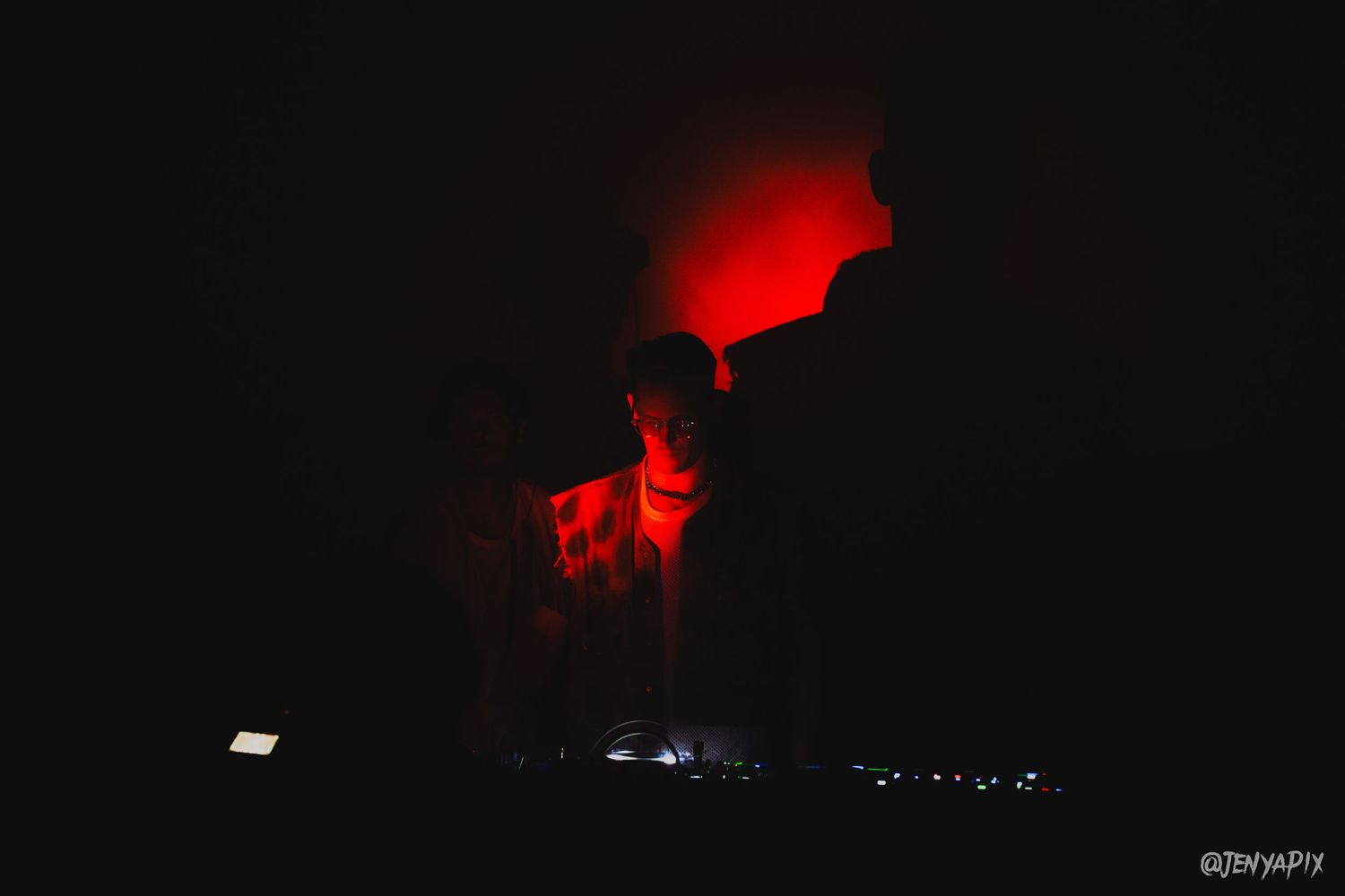 Silhouetted figure performing against dramatic red lighting in dark venue.