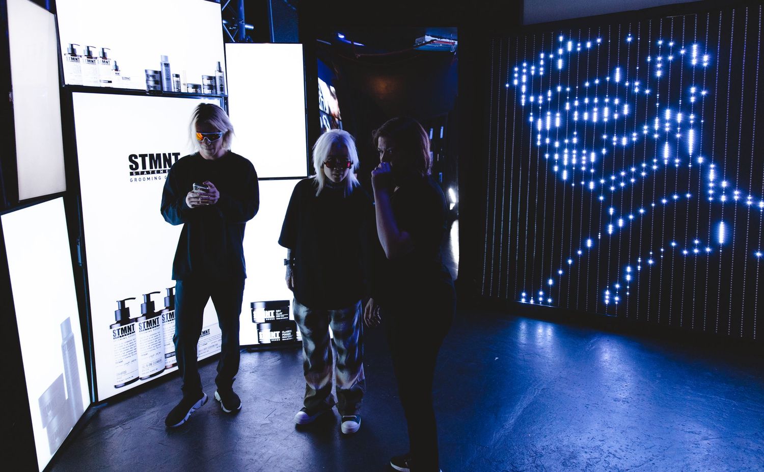 People viewing retail displays in dimly lit showroom with blue lighting accents.