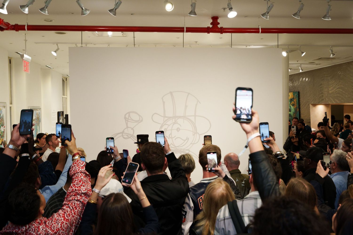 Crowd of people holding up phones to capture something on a white gallery wall.