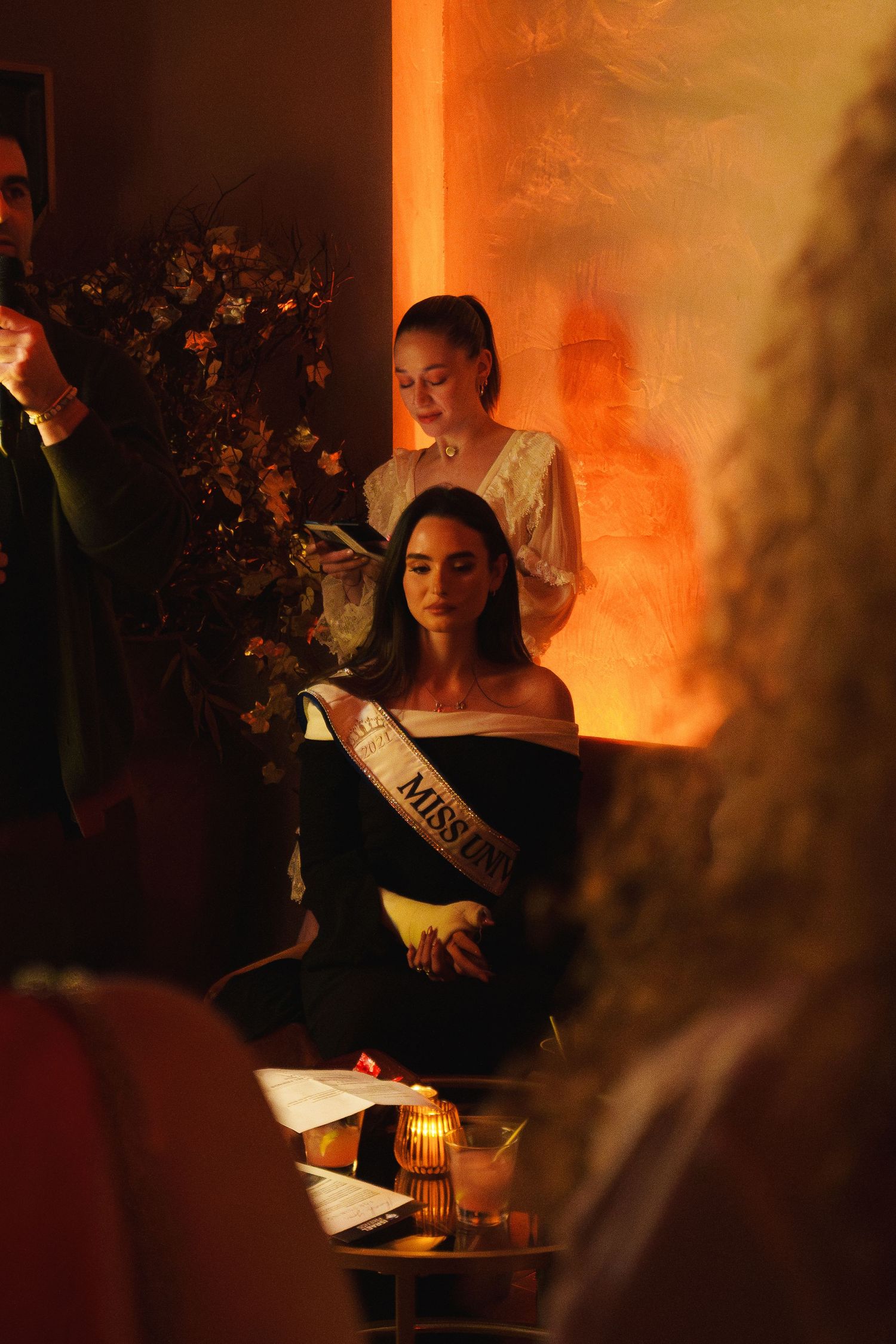 Event attendees at a candlelit gathering with warm orange lighting and floral decorations.