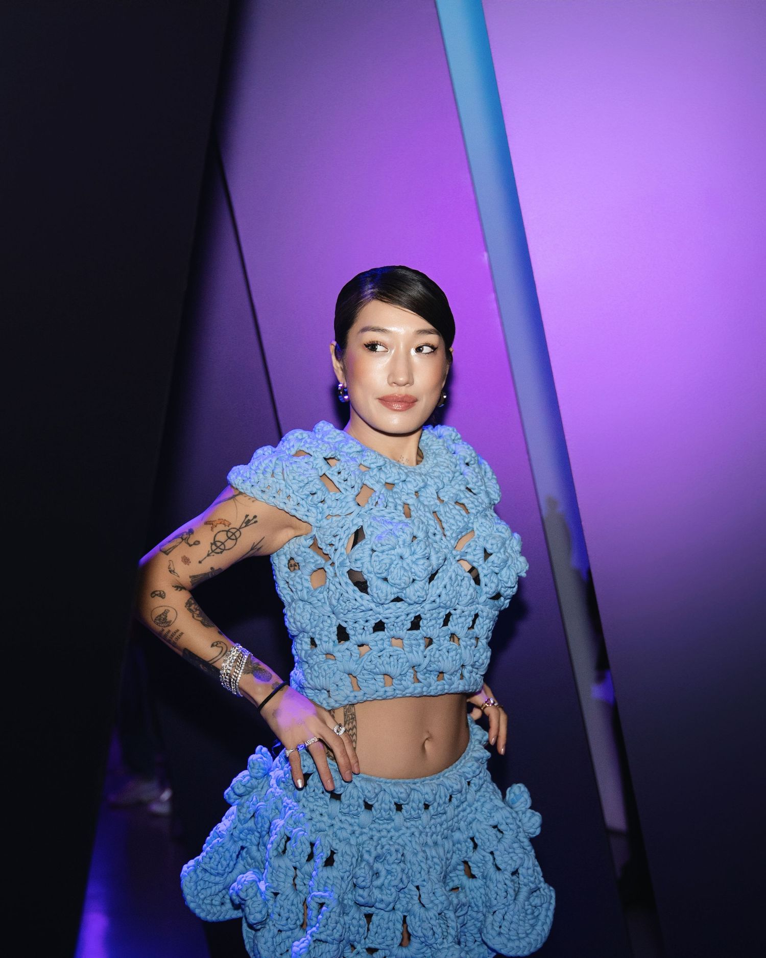 Person wearing light blue crochet two-piece outfit against purple backdrop.