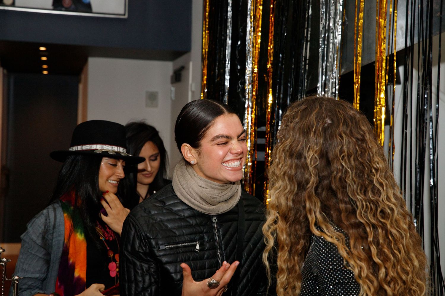 People engaged in animated conversation at a social gathering with festive decorations.