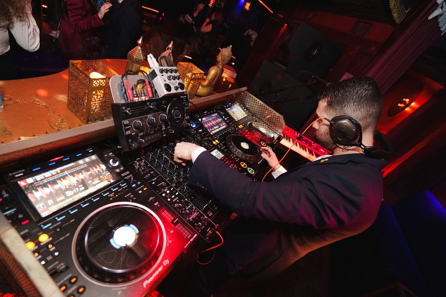 DJ performing at a nightclub mixing desk with professional equipment in dark red lighting.
