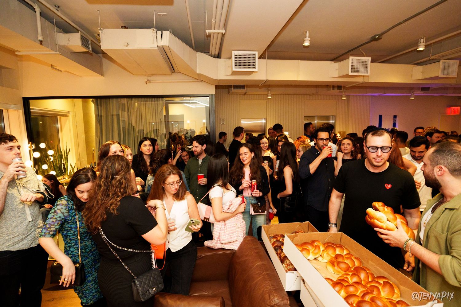 Crowd gathering around a food table at an indoor social event.