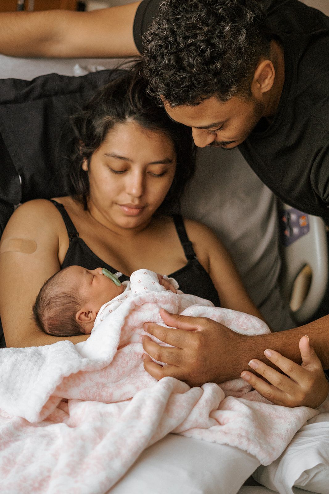 An intimate moment captured of new parents cradling their newborn baby wrapped in white.