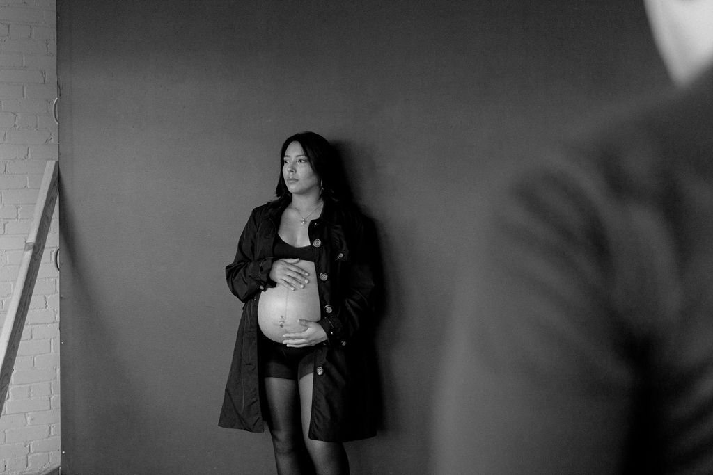 Artistic black and white maternity portrait against dark wall.