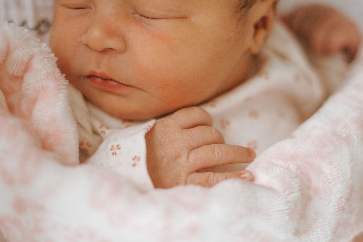 Close up of a sleeping newborn baby wrapped in pink floral blanket.