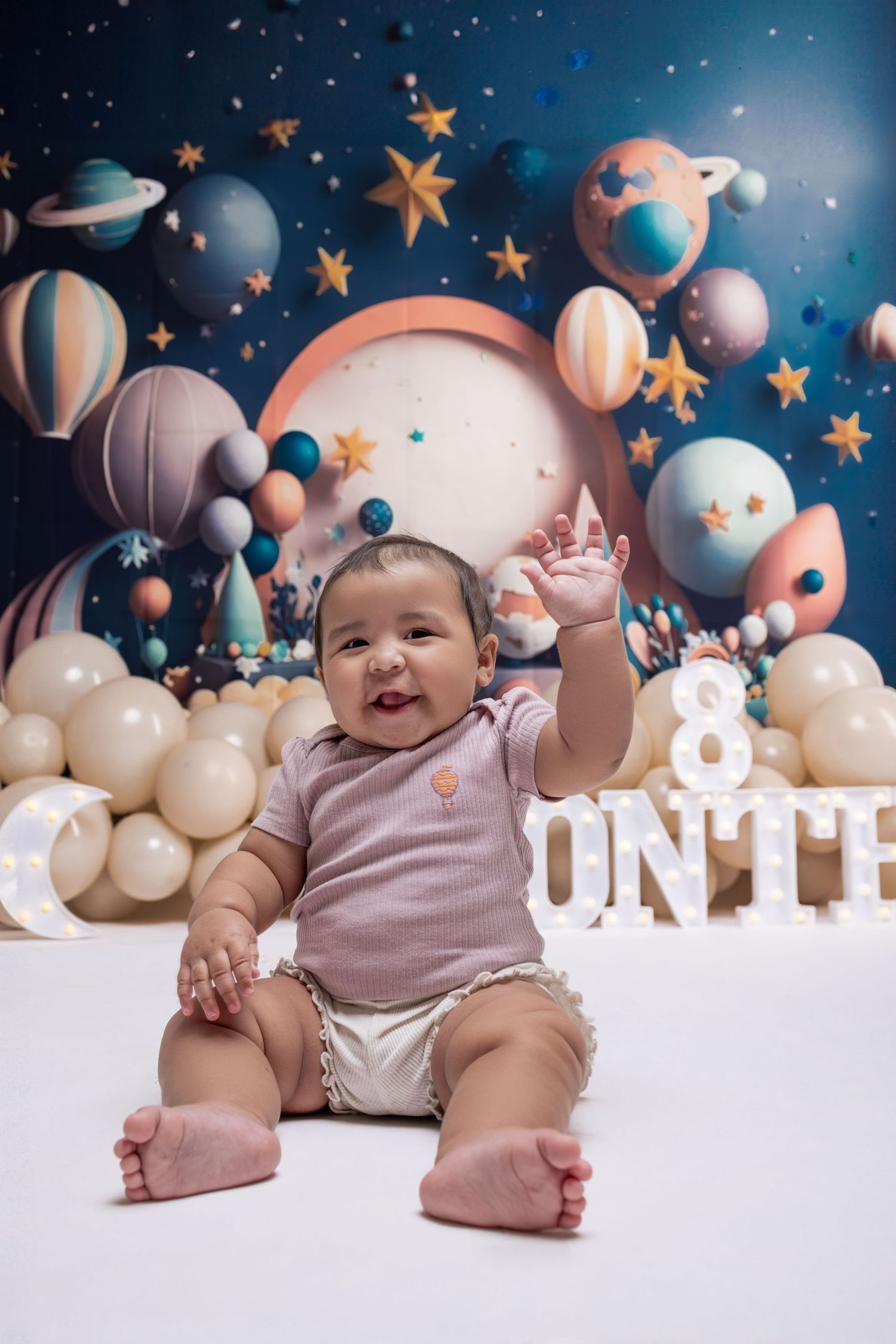 A happy baby sits among celestial-themed decorations with balloons and stars.