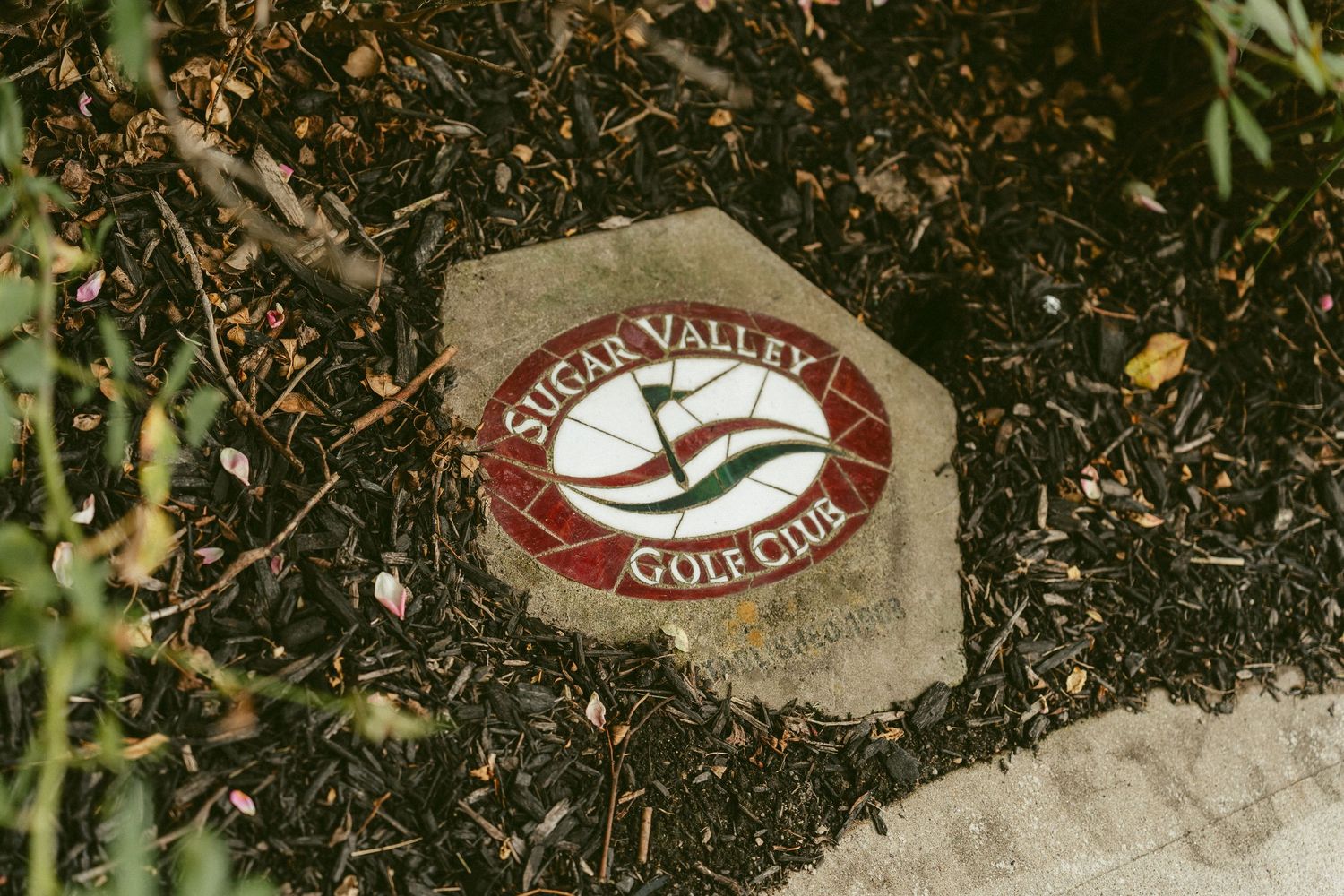 A golf ball sits on a brown dirt surface near fallen leaves and grass with a golf club logo visible in the background. Located in Bellbrook,