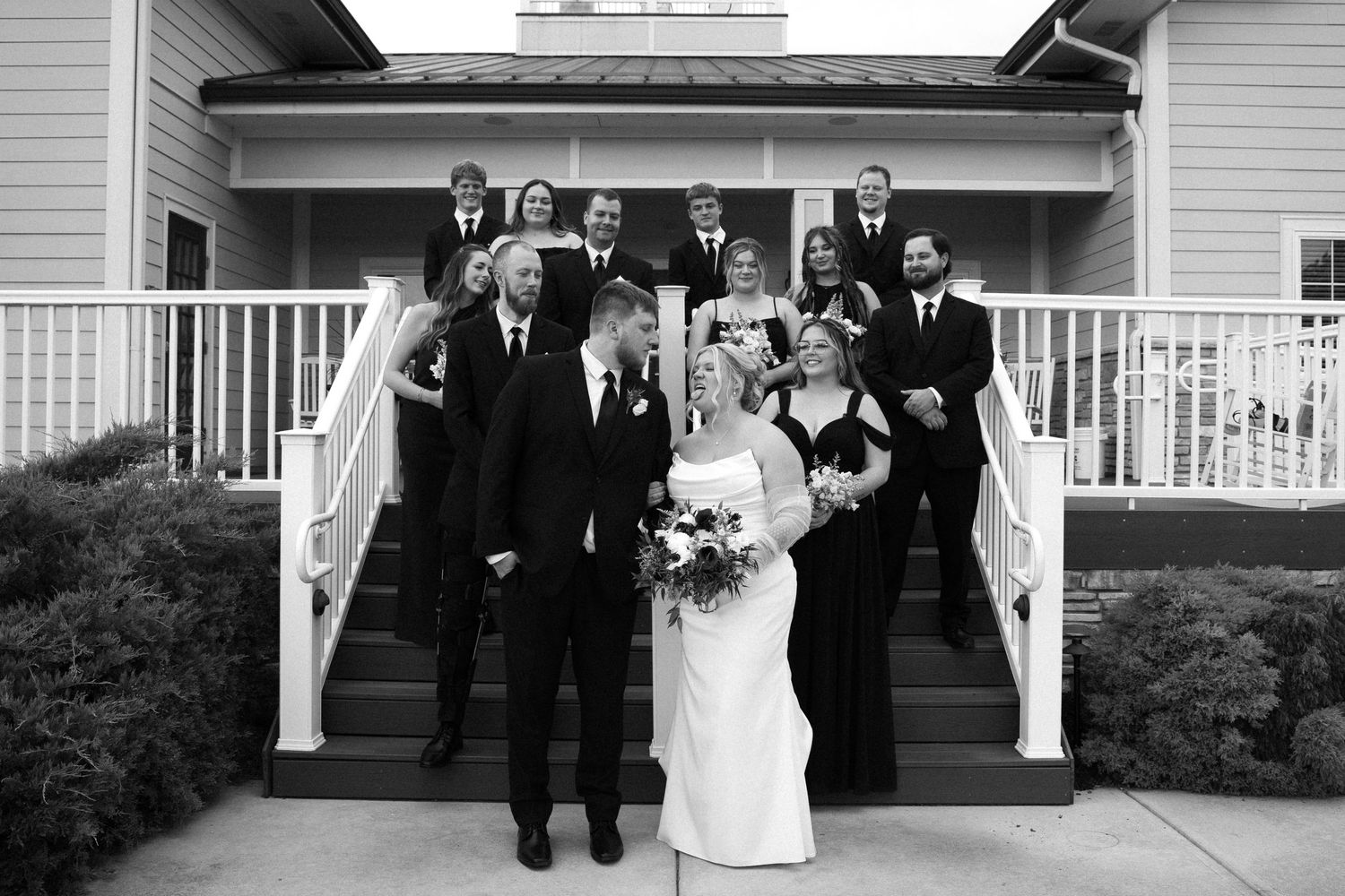 Wedding party poses together on white porch steps of elegant farmhouse venue during formal celebration. Located in Bellbrook, Ohio.