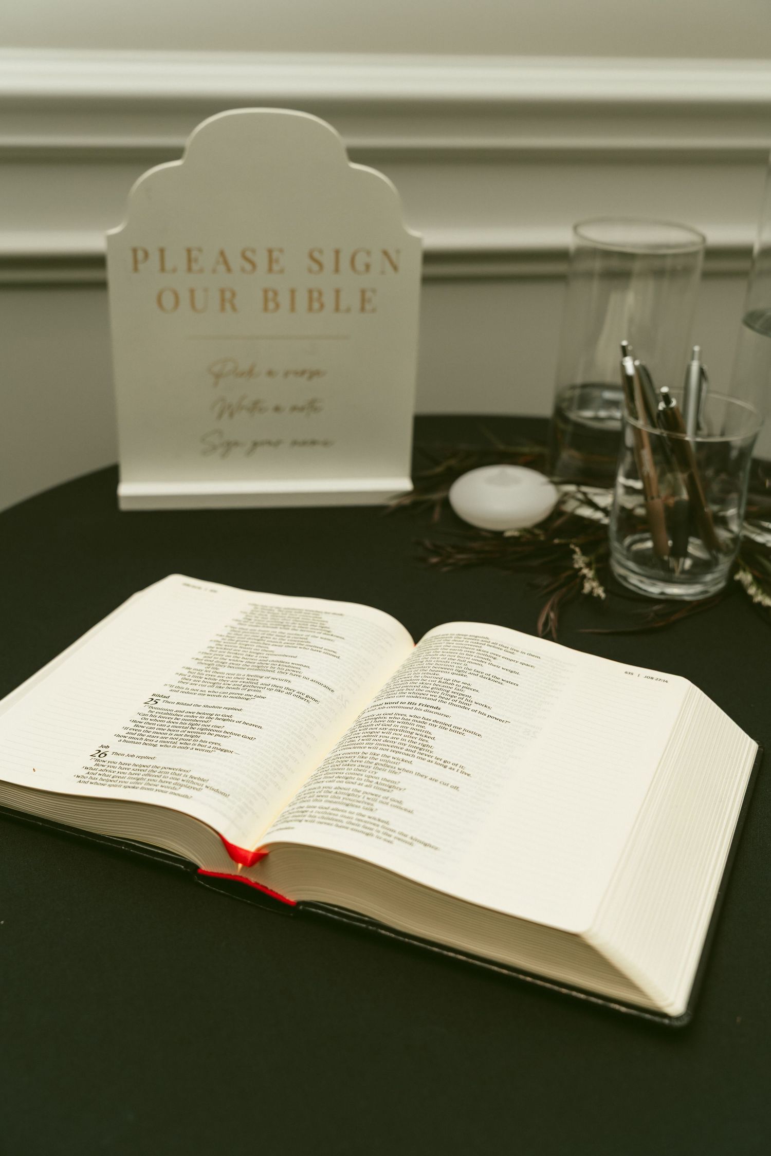An open Bible displayed on a dark table with a 'Please Sign' and 'Our Bible' sign visible in the background. Located in Bellbrook, Ohio.