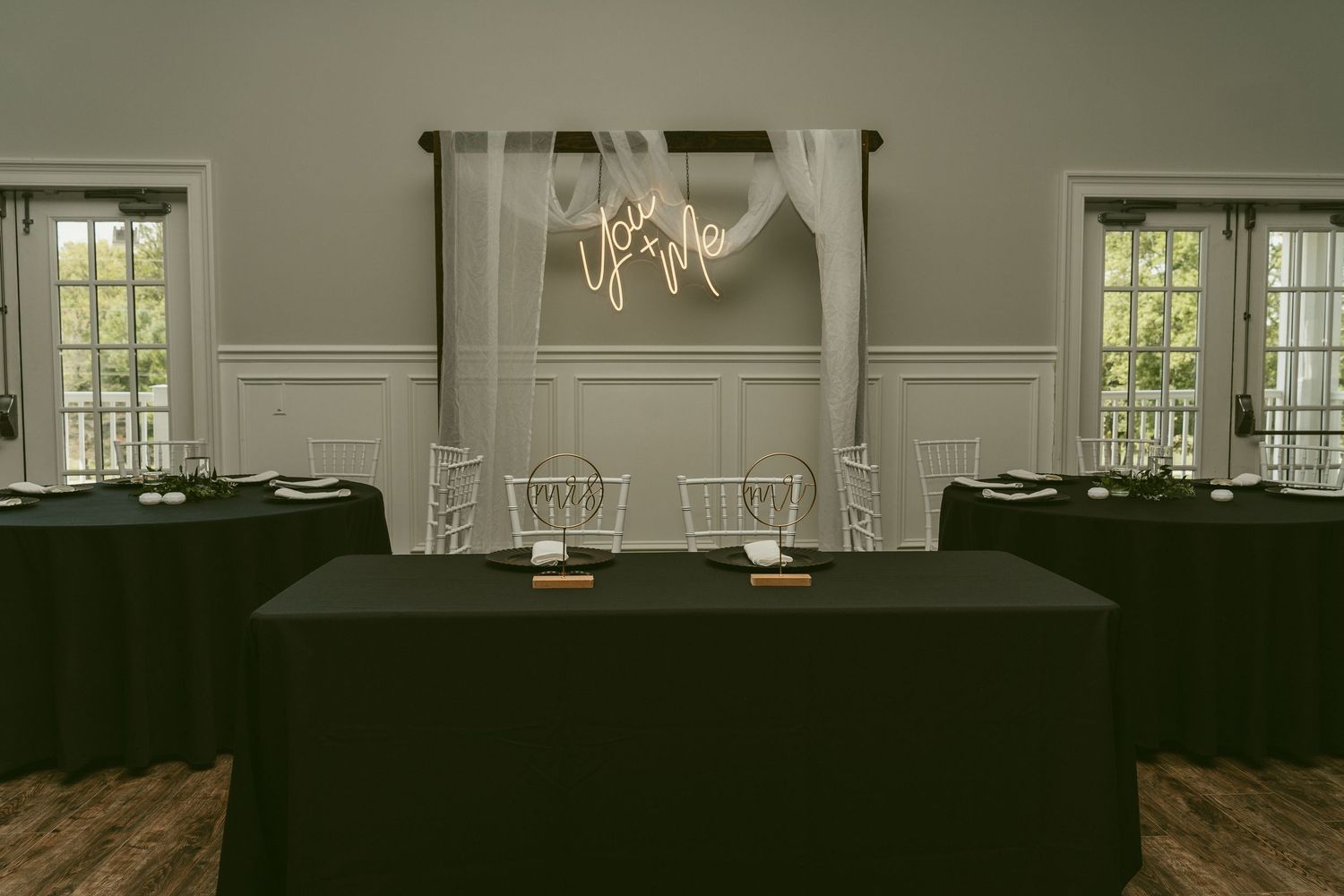 Interior view of an elegant white ballroom with crystal chandeliers and large windows letting in natural light. Located in Bellbrook, Ohio.