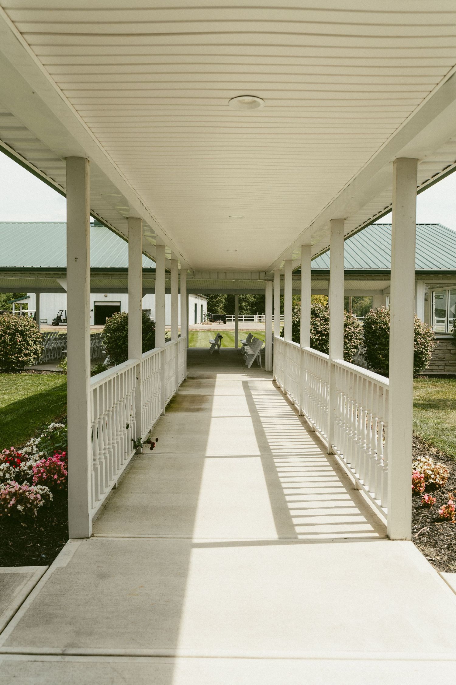 A covered walkway with white columns and railings leads through a garden with blooming flowers and green landscaping. Located in Bellbrook.