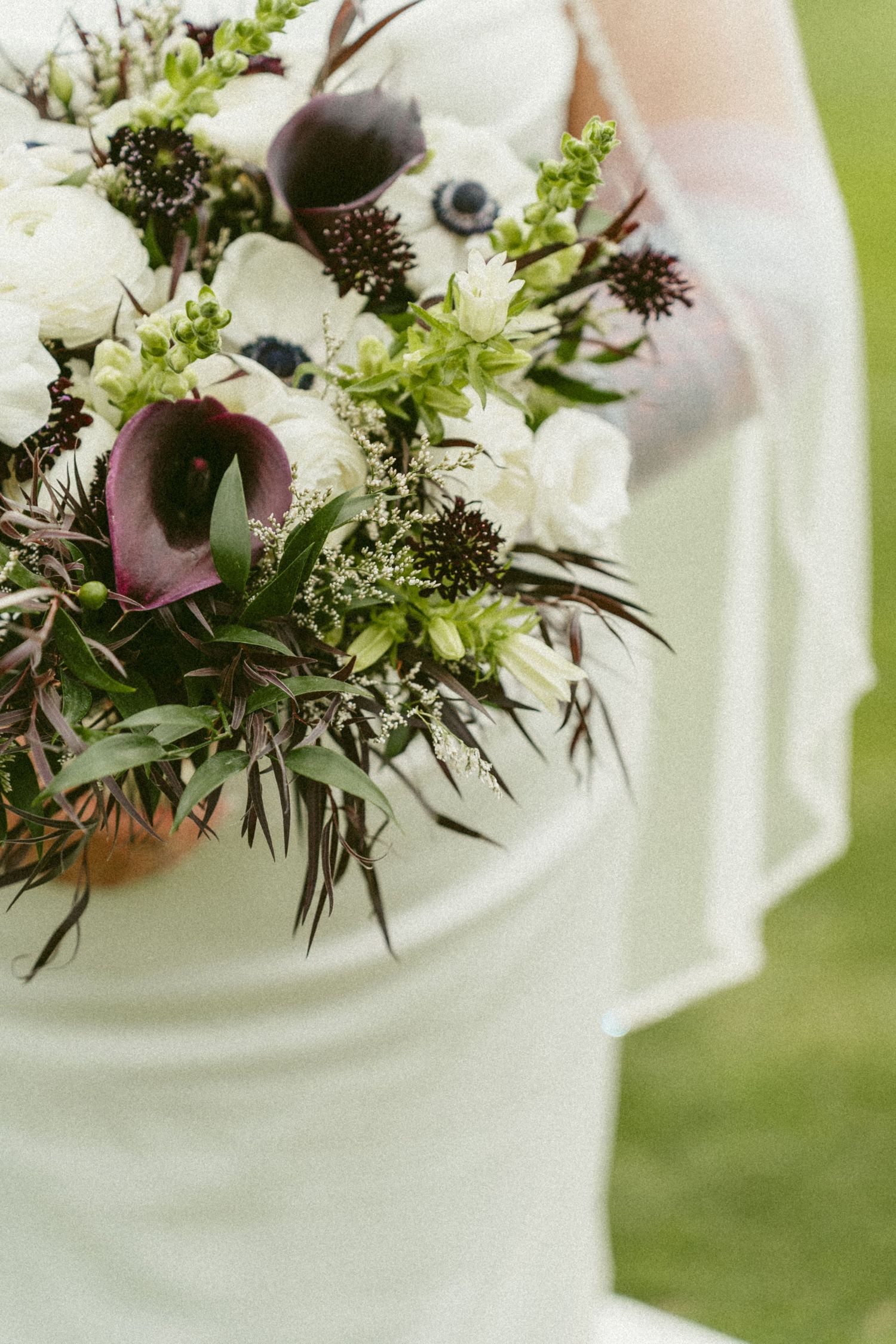 A delicate white and purple wedding bouquet featuring calla lilies and wildflowers against a soft green background. Located in Bellbrook, Oh