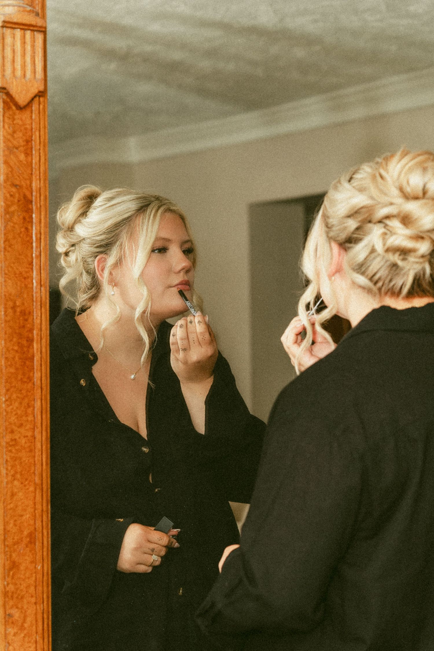 Reflections in a mirror show a bride in black clothing with blonde hair applying makeup. Located in Bellbrook, Ohio.