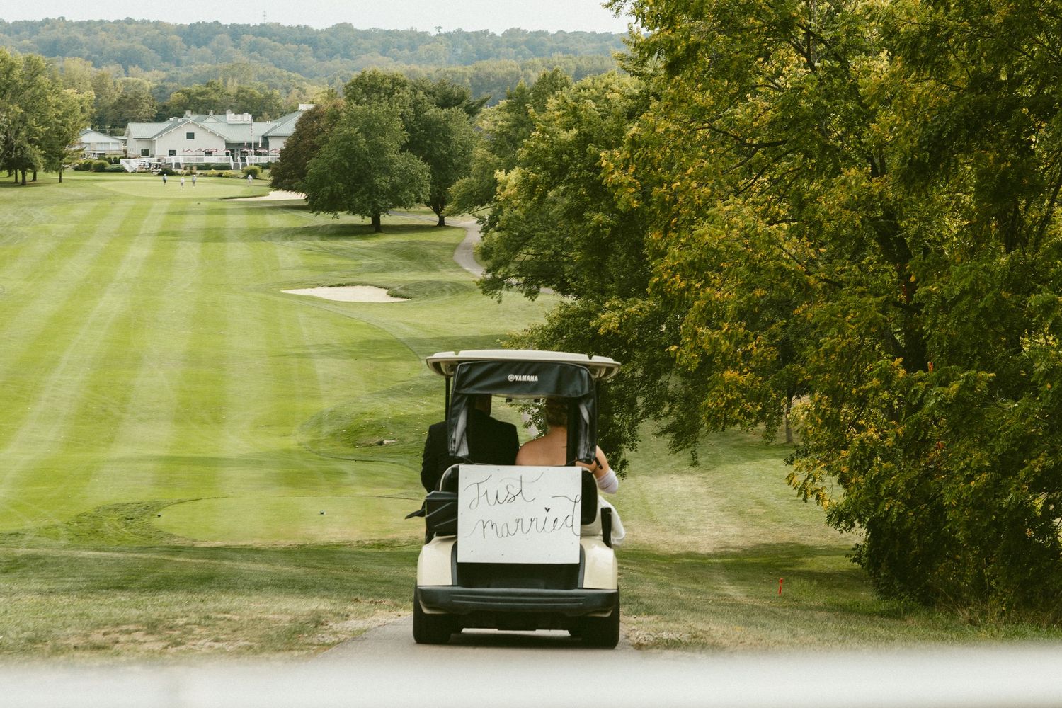 Golf cart with 'Just Married' sign drives along scenic tree-lined fairway at country club golf course. Located in Bellbrook, Ohio.