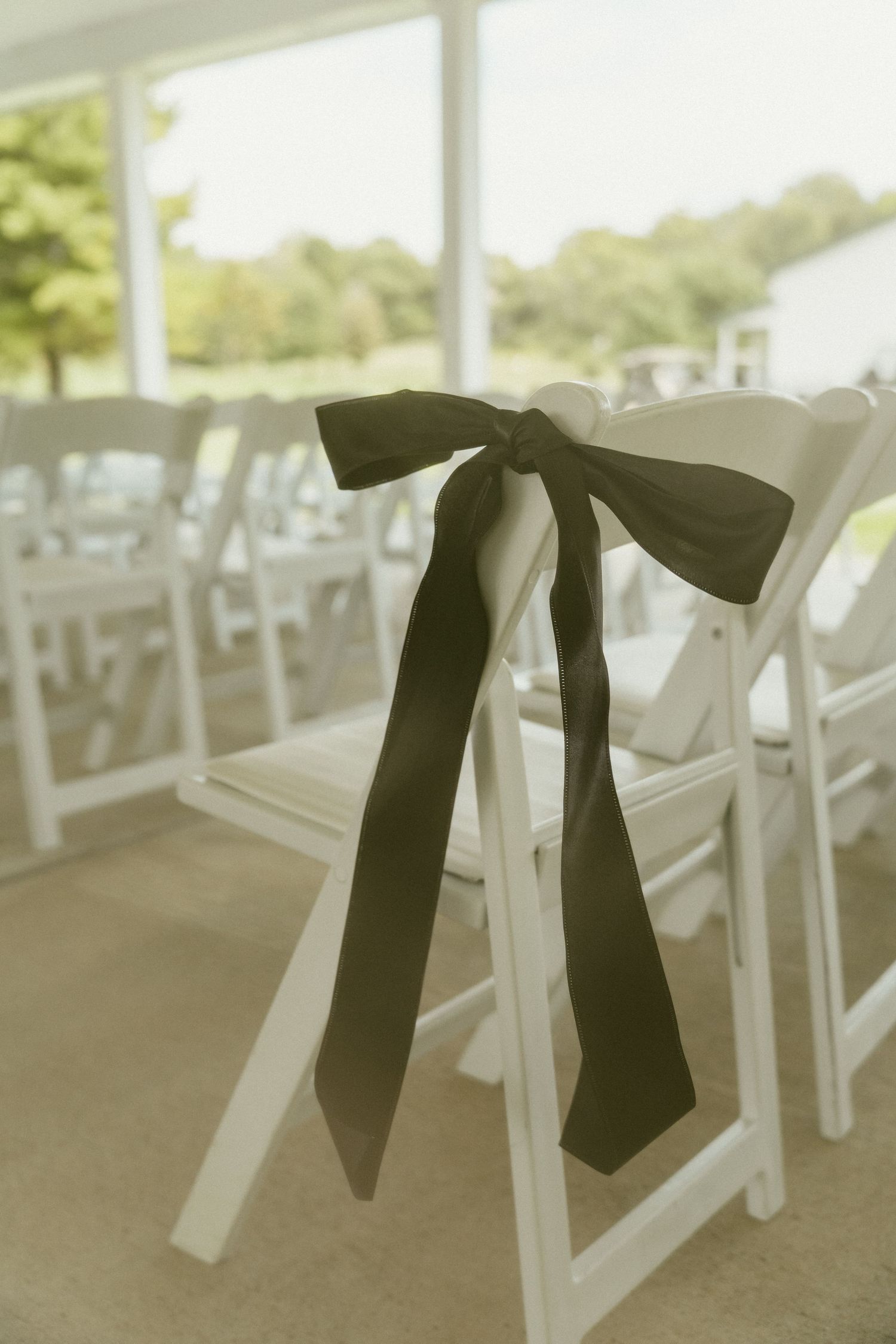 Black ribbons tied to white folding chairs create an elegant wedding ceremony seating arrangement outdoors. Located in Bellbrook, Ohio.