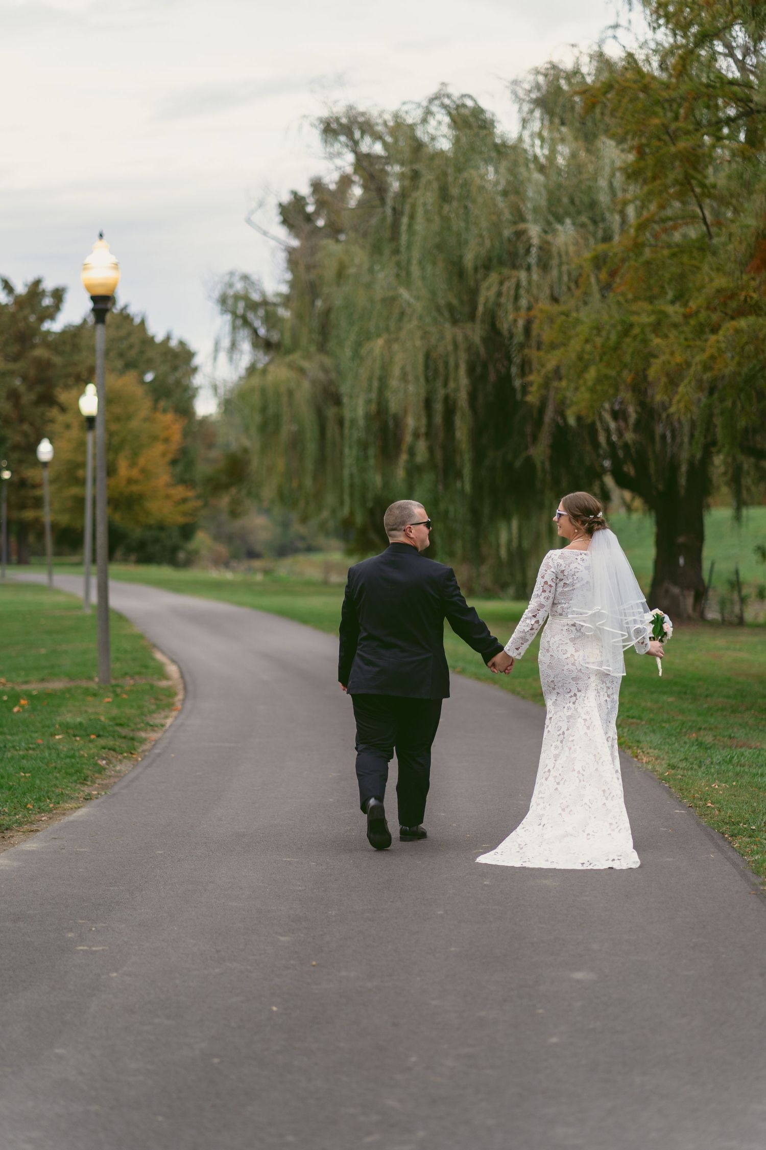 A couple in wedding attire walking down a tree-lined path in autumn, shown in a sequence of four photos moving away. Located in Dayton, Ohio