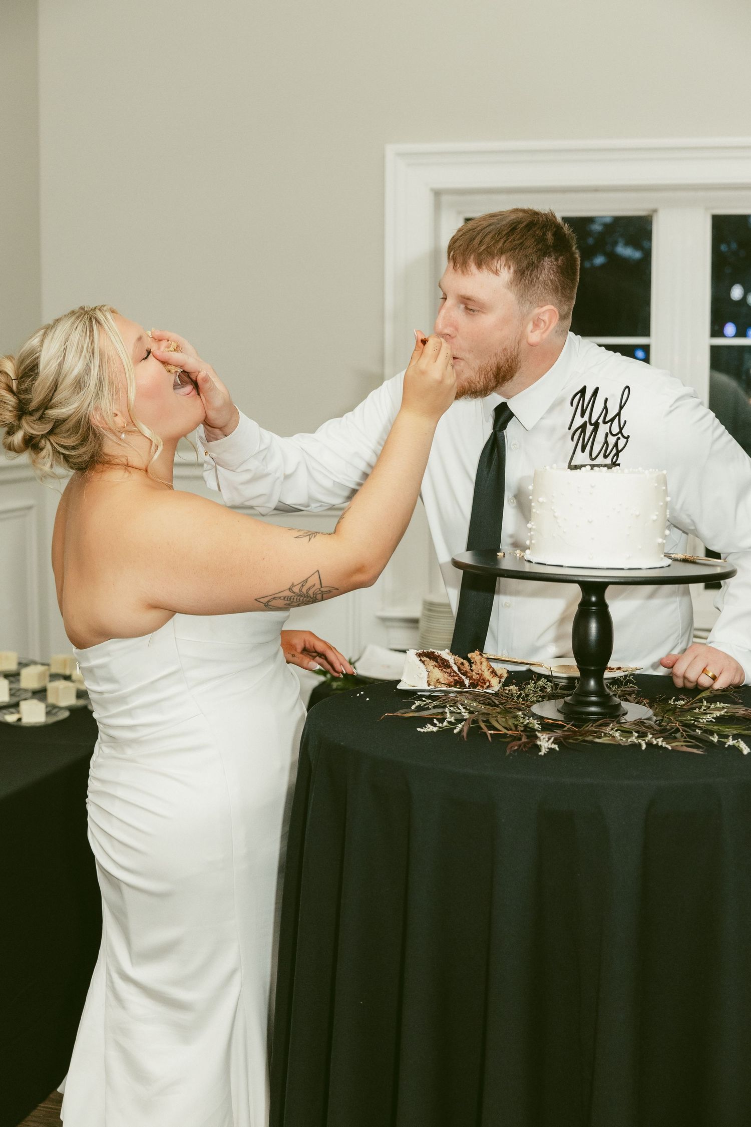 A couple playfully smashes wedding cake into each others faces during their reception celebration. Located in Bellbrook, Ohio.