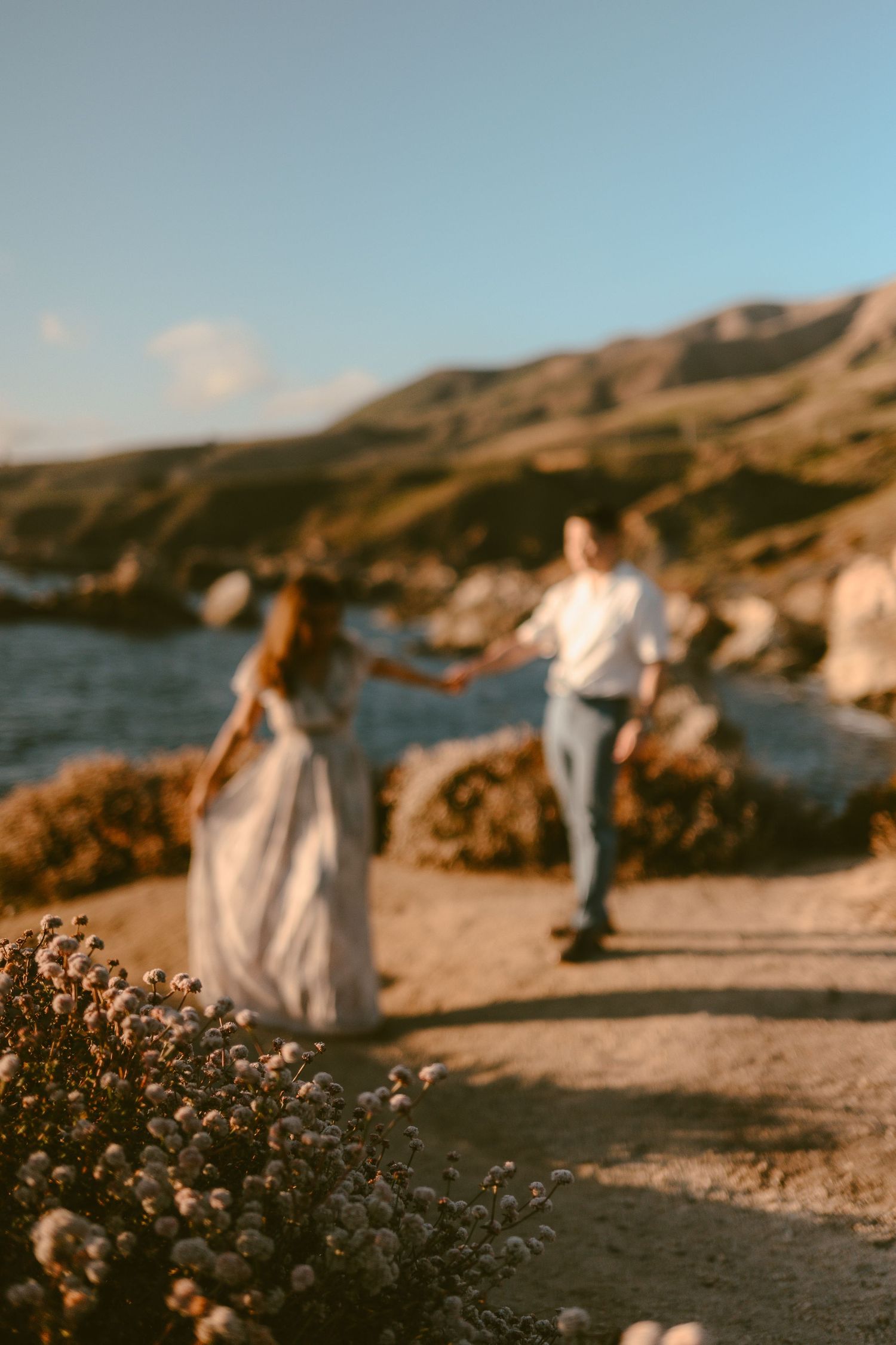 Couple holding hands walking along a coastal path at golden hour with ocean views.