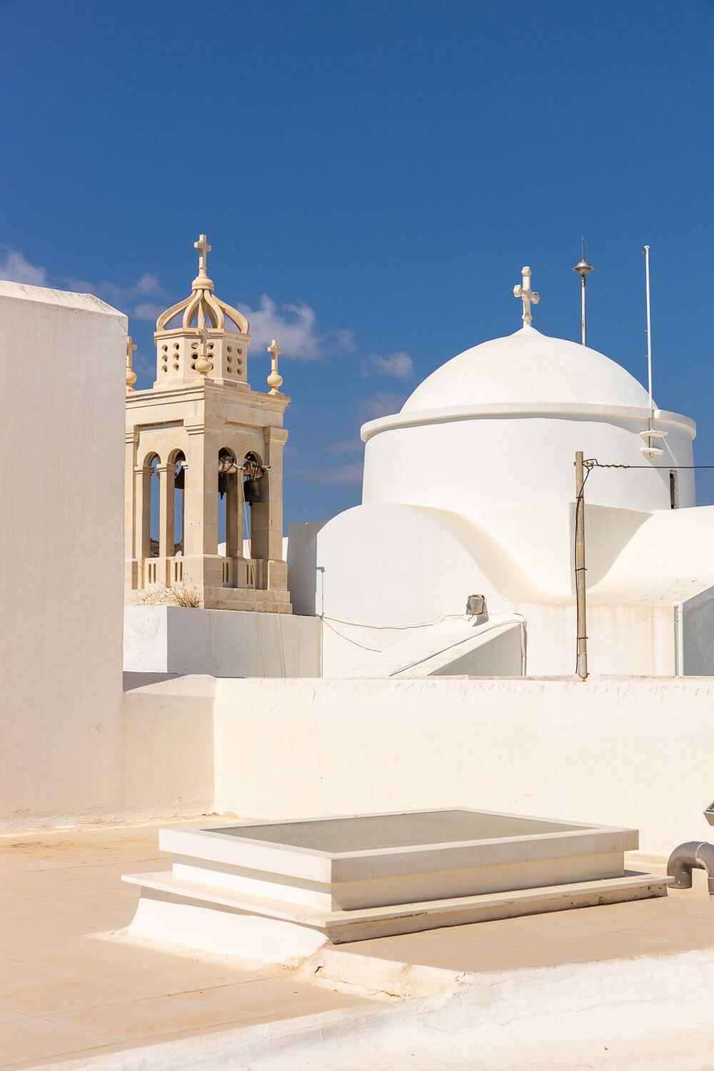 White domed church buildings with crosses and bell towers against bright blue sky in Greek Orthodox architectural style in Paros Greece