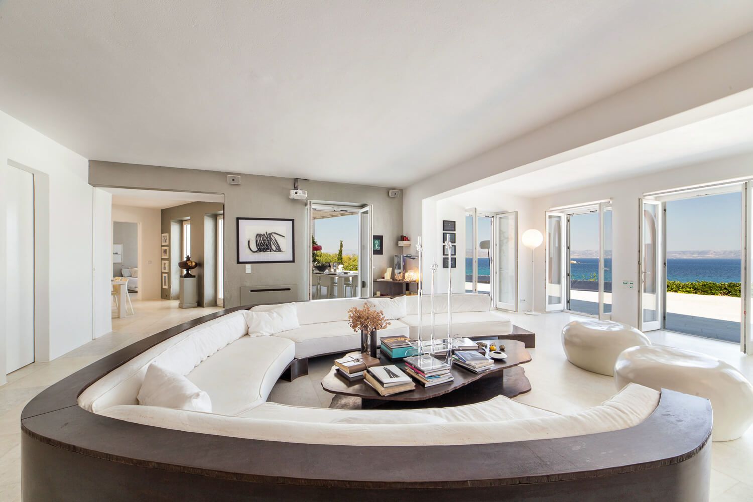 Luxurious circular white sofa in modern living room with ocean views and floor-to-ceiling windows.