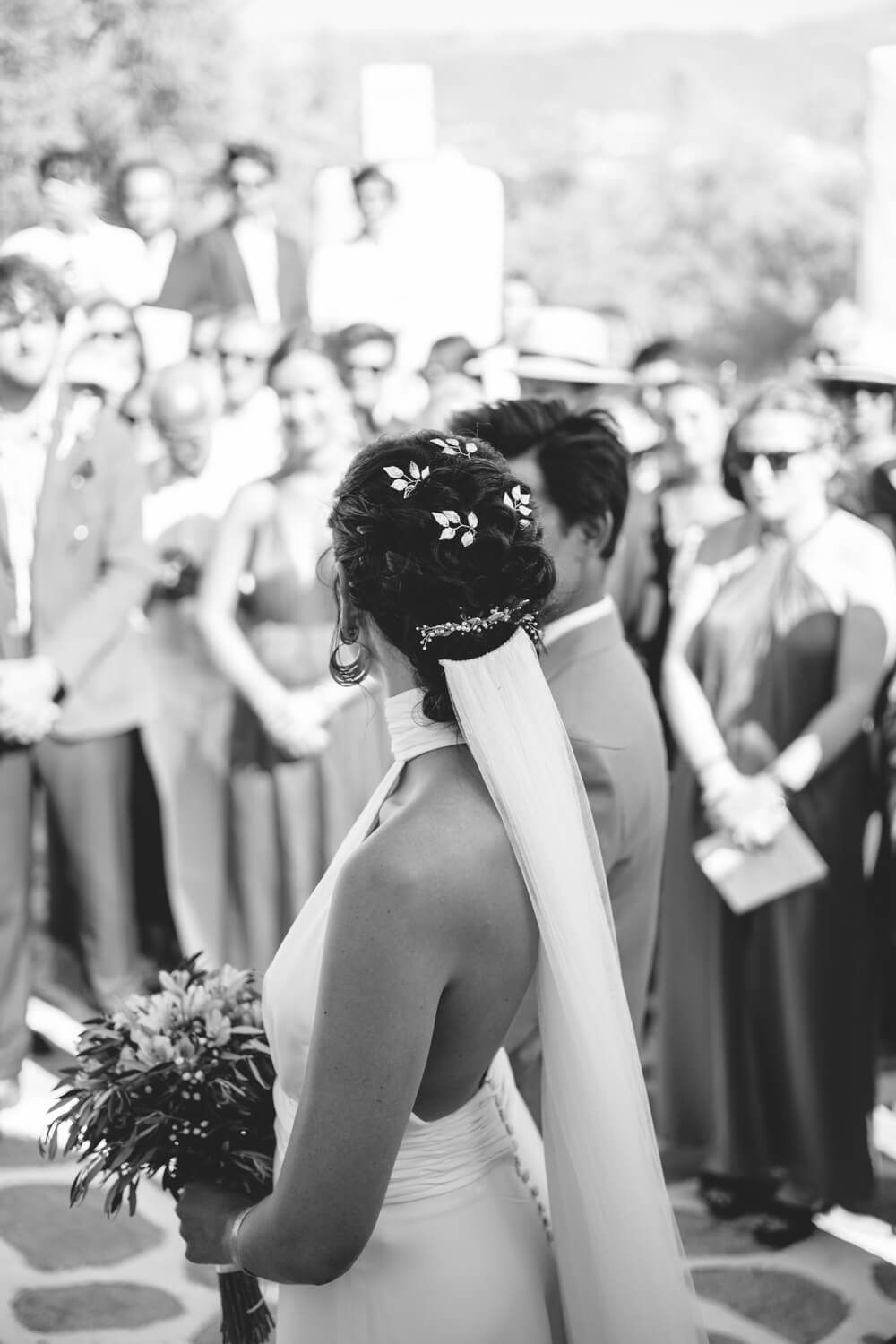 Bride with floral hair accessories holding bouquet walks toward wedding guests.