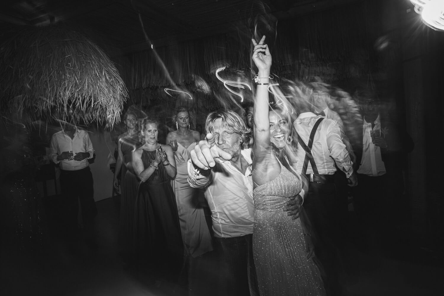 Black and white photo of bride and groom dancing joyfully surrounded by wedding guests.