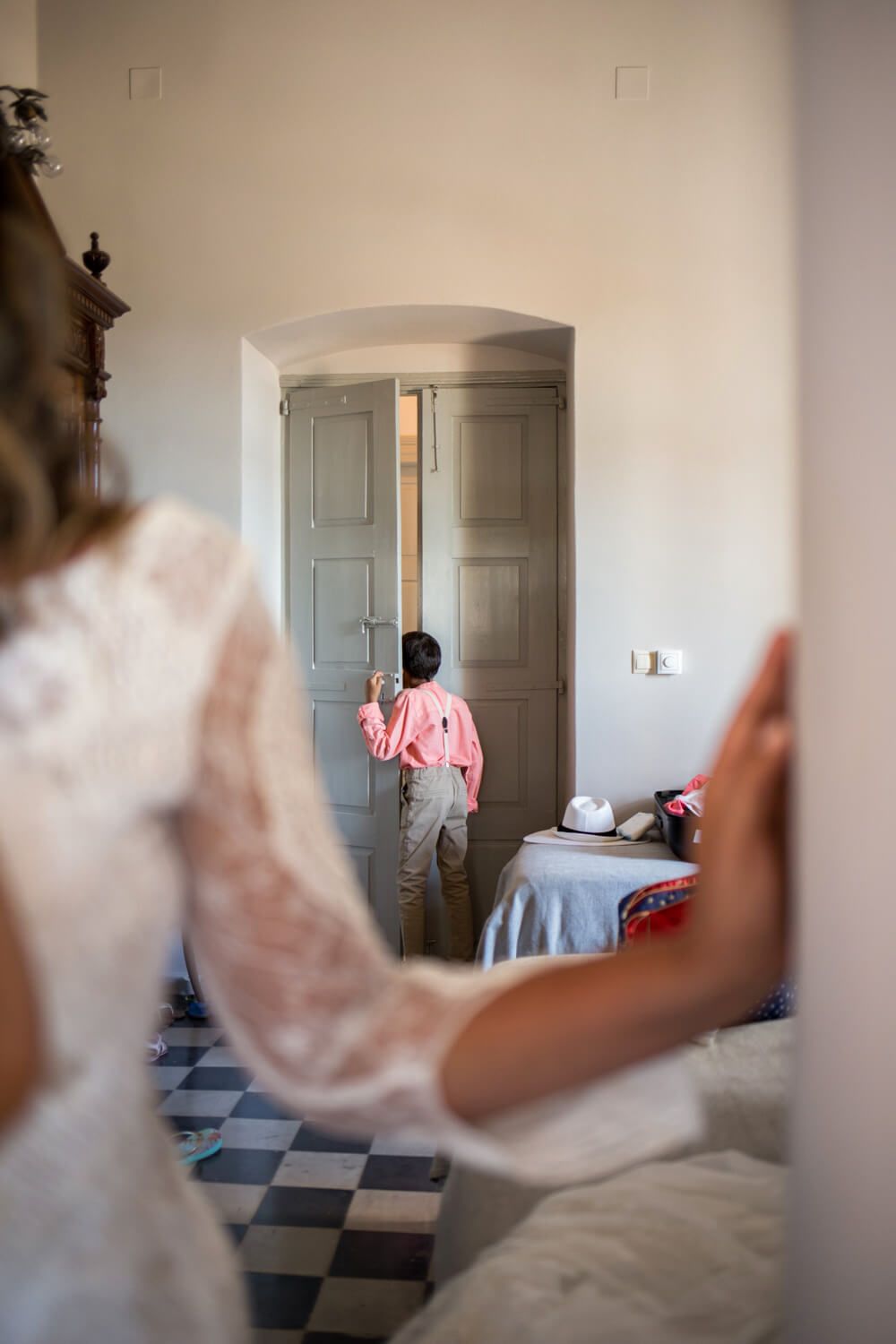 Boy in pink shirt opening gray door at wedding venue with bride in lace dress in foreground.