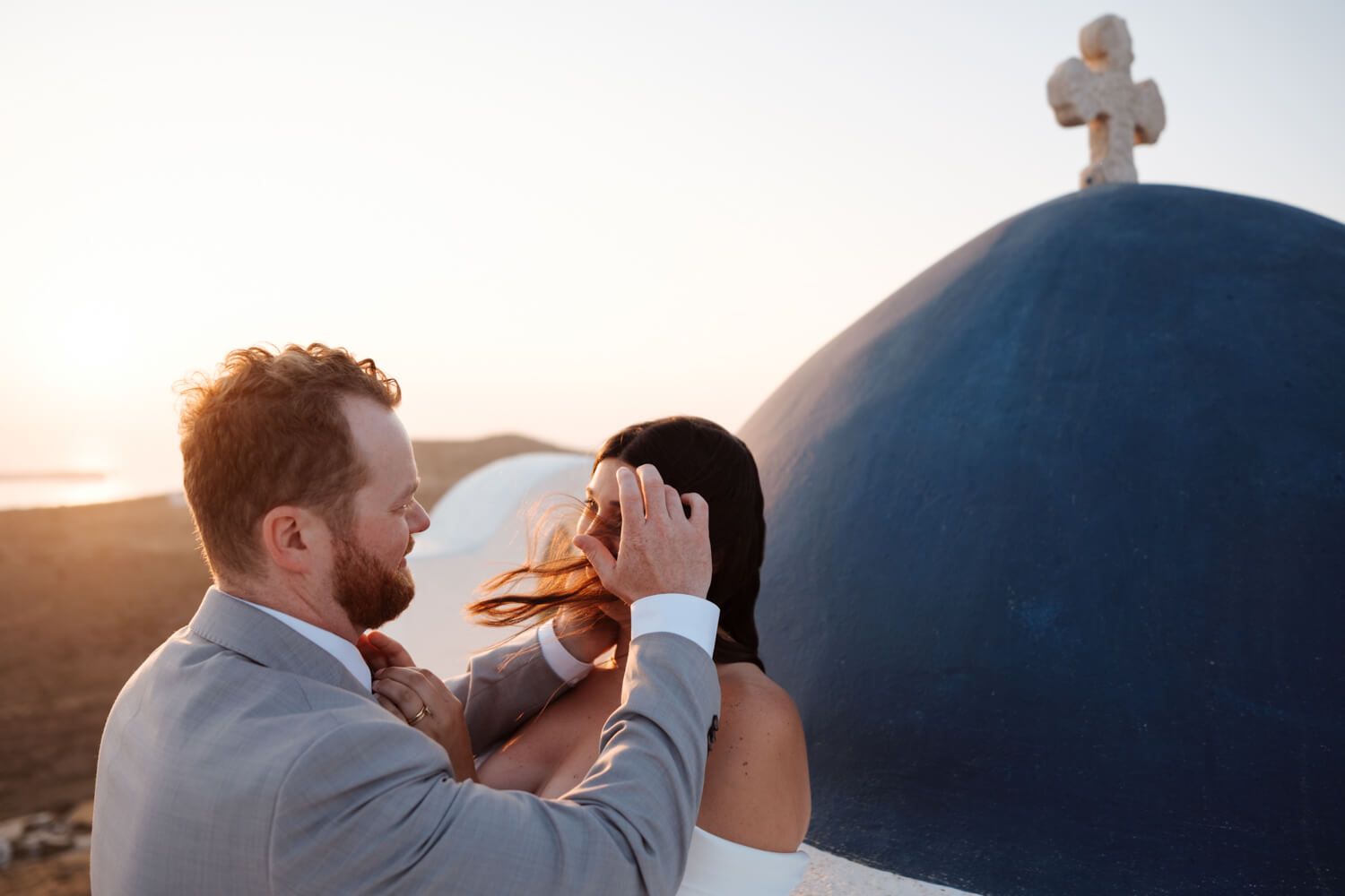 Couple sharing romantic moment at sunset near iconic blue domed church in Santorini Greece during wedding.