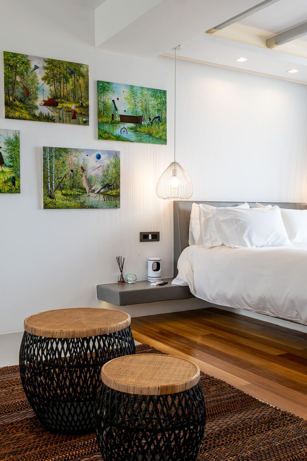 Bedroom with hardwood floors features nature artwork, white bedding, and round wooden side tables with black bases.
