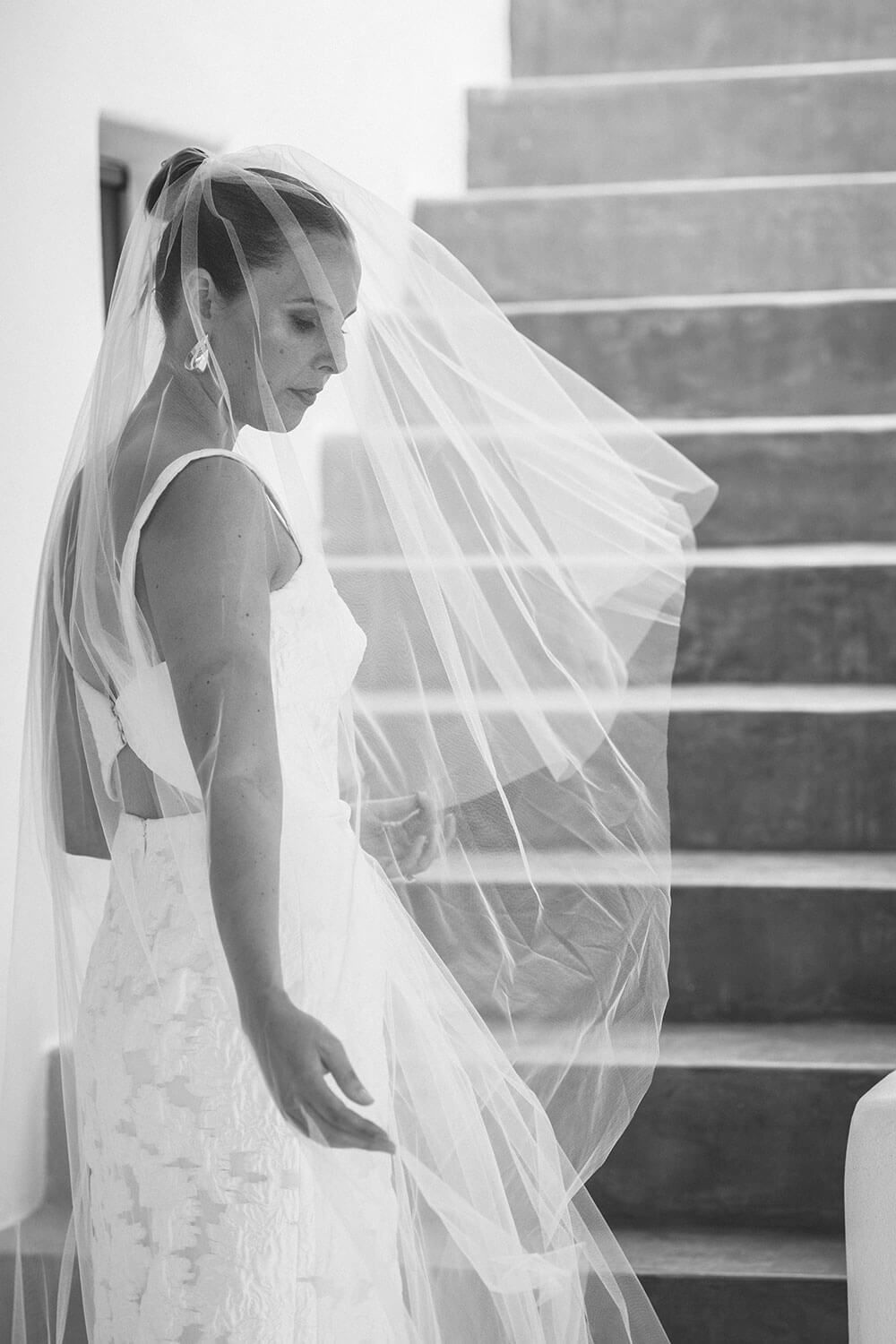 A bride in a flowing wedding dress and veil poses in black and white photography in Paros Greece