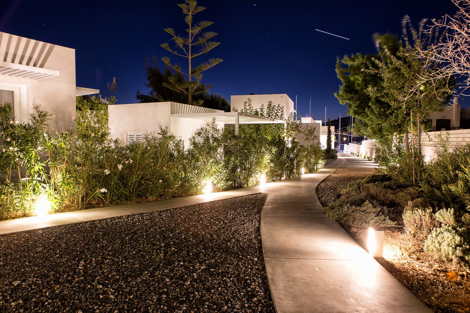 Illuminated outdoor pathway with modern architectural elements and landscaping features at night.