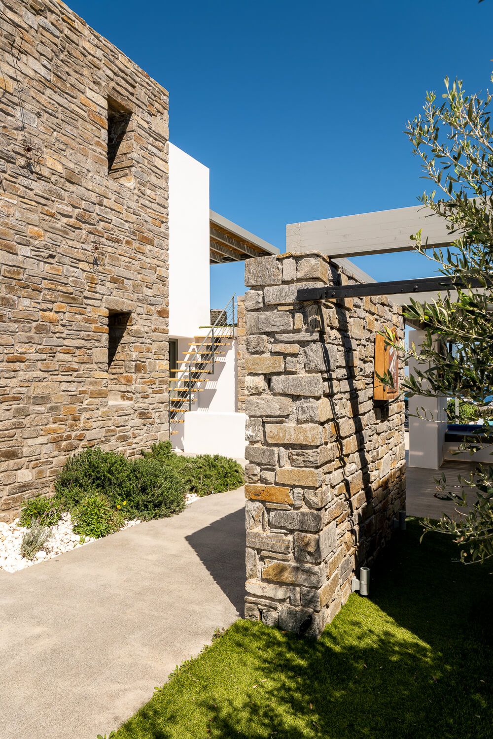 Modern stone wall walkway with white architectural elements creates a contemporary outdoor passage under bright blue sky.