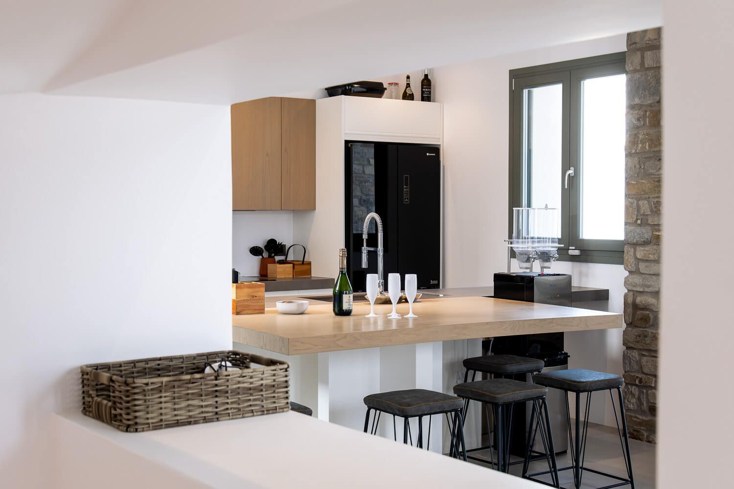 Kitchen with wooden countertop, black bar stools, and woven storage basket features sleek cabinet design.
