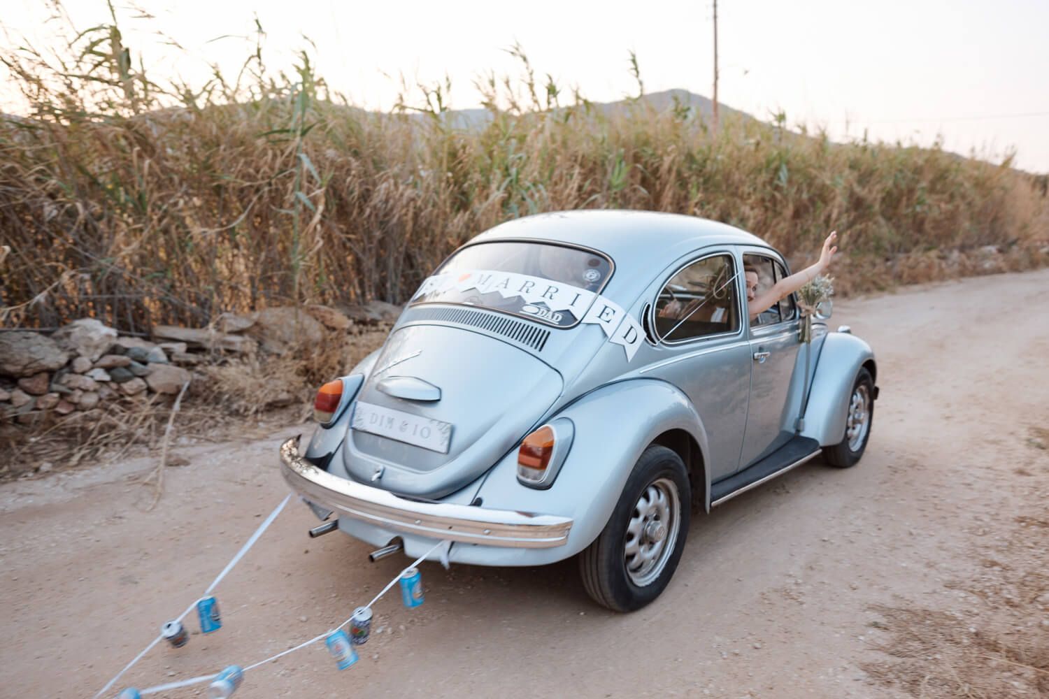 Bride waiving from a vintage wedding car in Paros