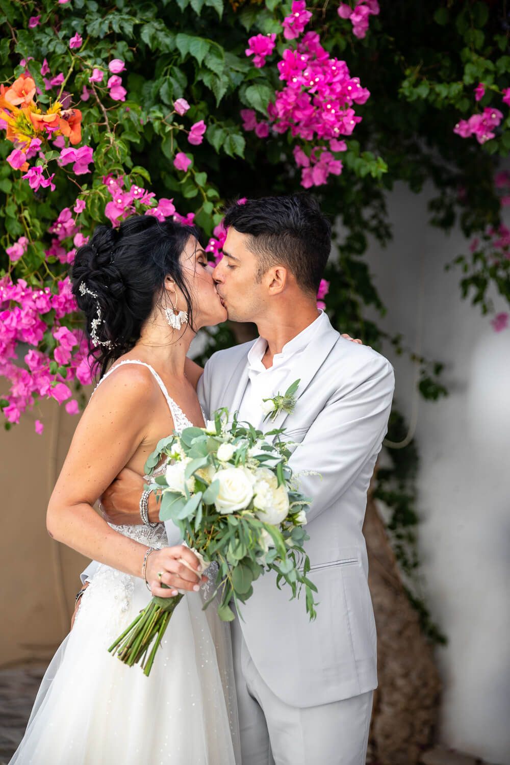 Groom kissing the bride's forehead under a blooming bougainvillea