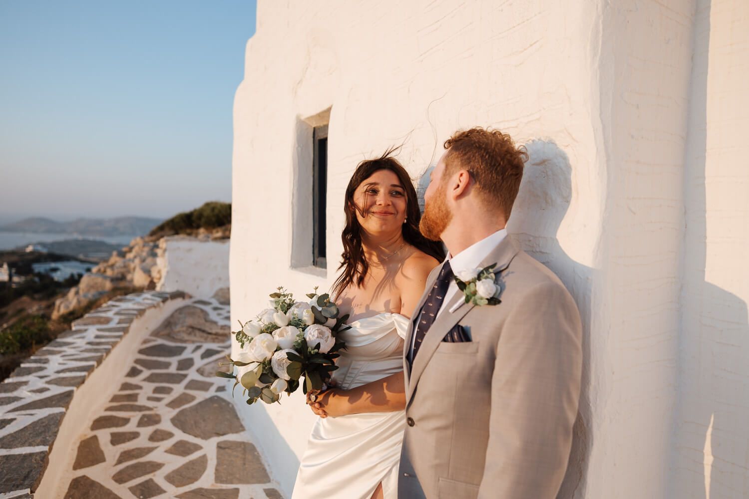 Newlyweds walking by a white chapel in Paros at dusk
