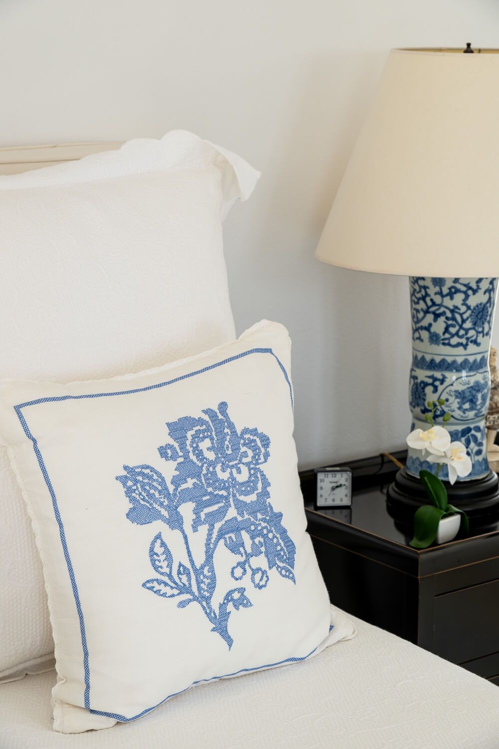White decorative pillows with delicate blue floral patterns arranged on a bed next to a table lamp with matching design.