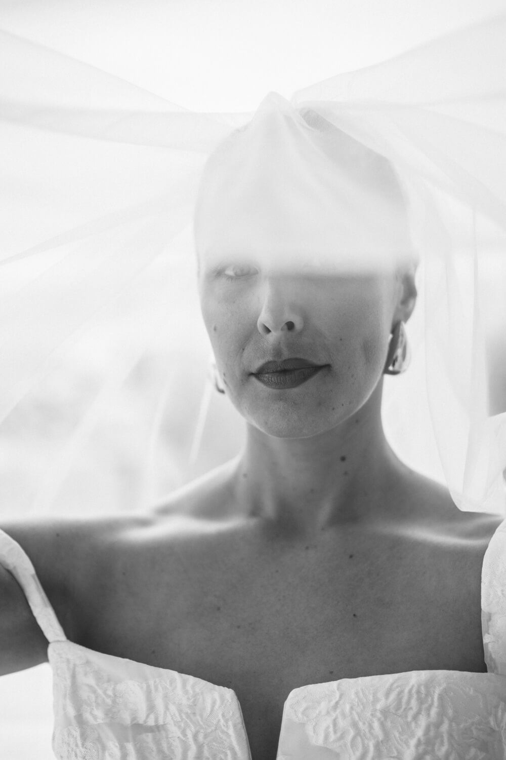 Black and white portrait of a bride with veil draped over her head, in Kolymbithres Paros.