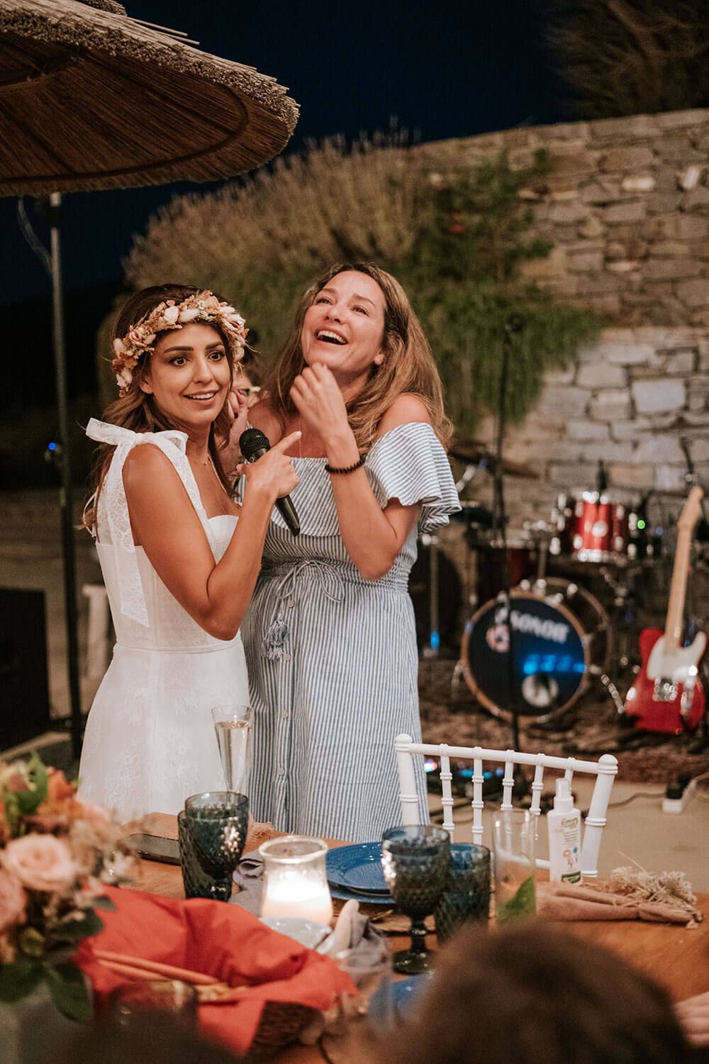 Two people share a joyful moment while sitting at a rustic outdoor dining table during sunset.