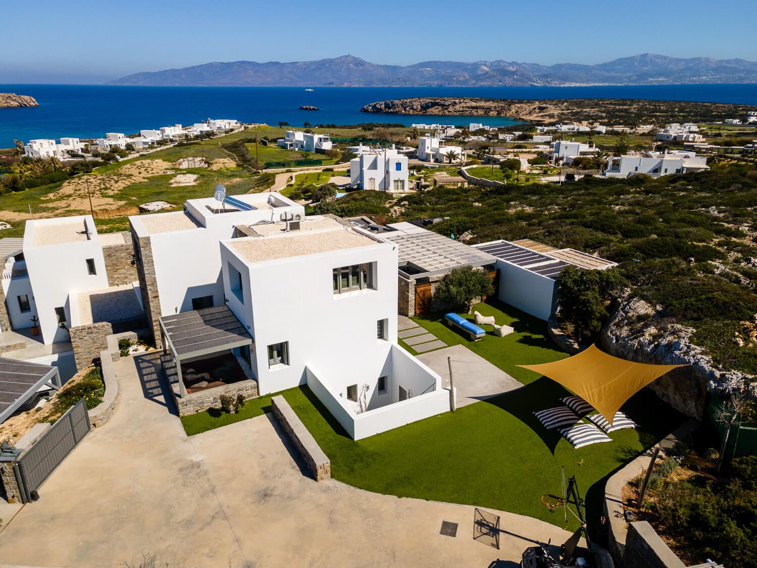 Aerial view of modern white luxury villas with green lawns overlooking the Mediterranean Sea and mountains in Greece.