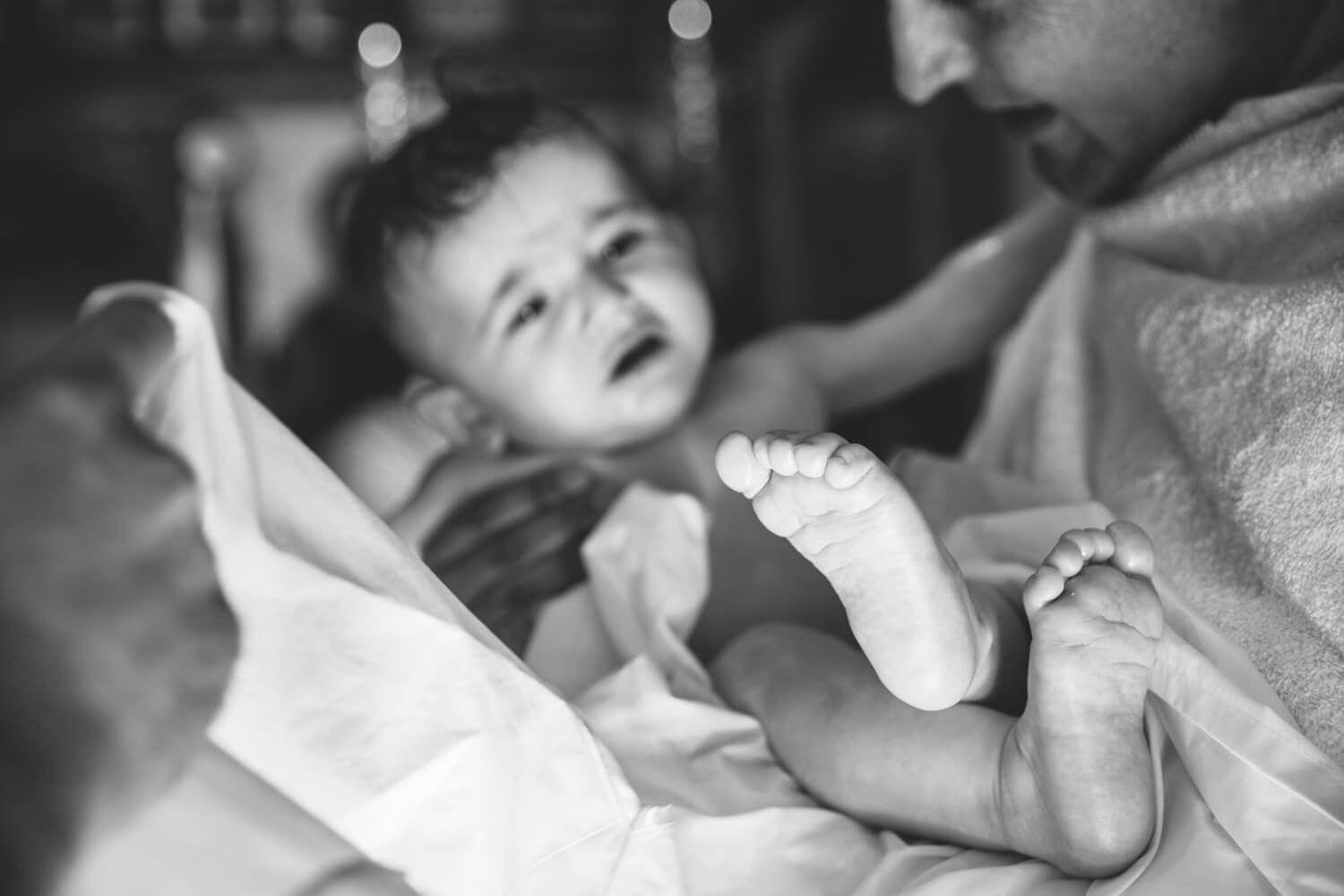 Black and white photo of a baby lying down with tiny feet in focus, during a baptism in Paros.