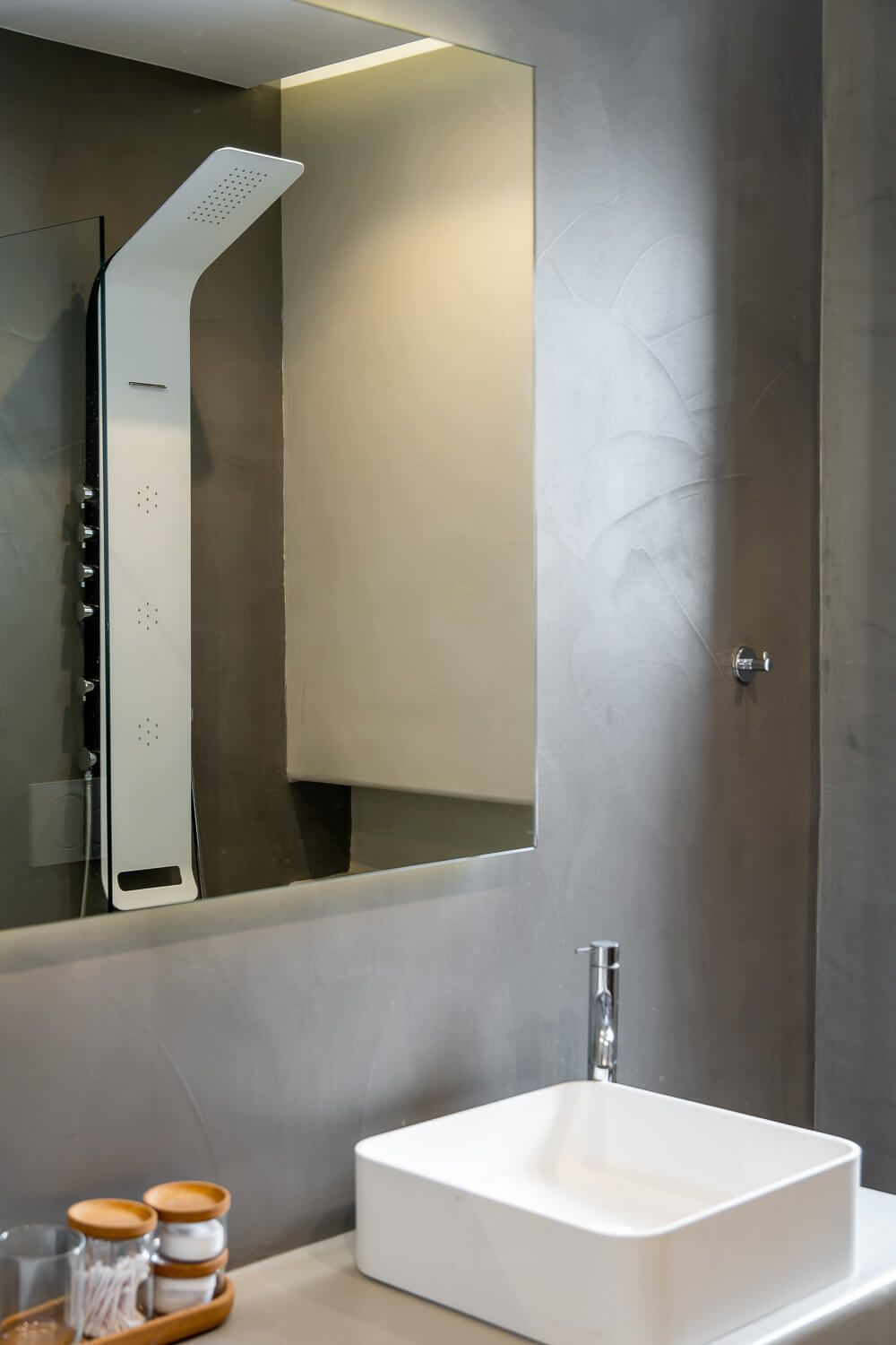 Modern bathroom interior with sleek white vessel sink, wall-mounted shower panel, and mirror with ambient lighting.