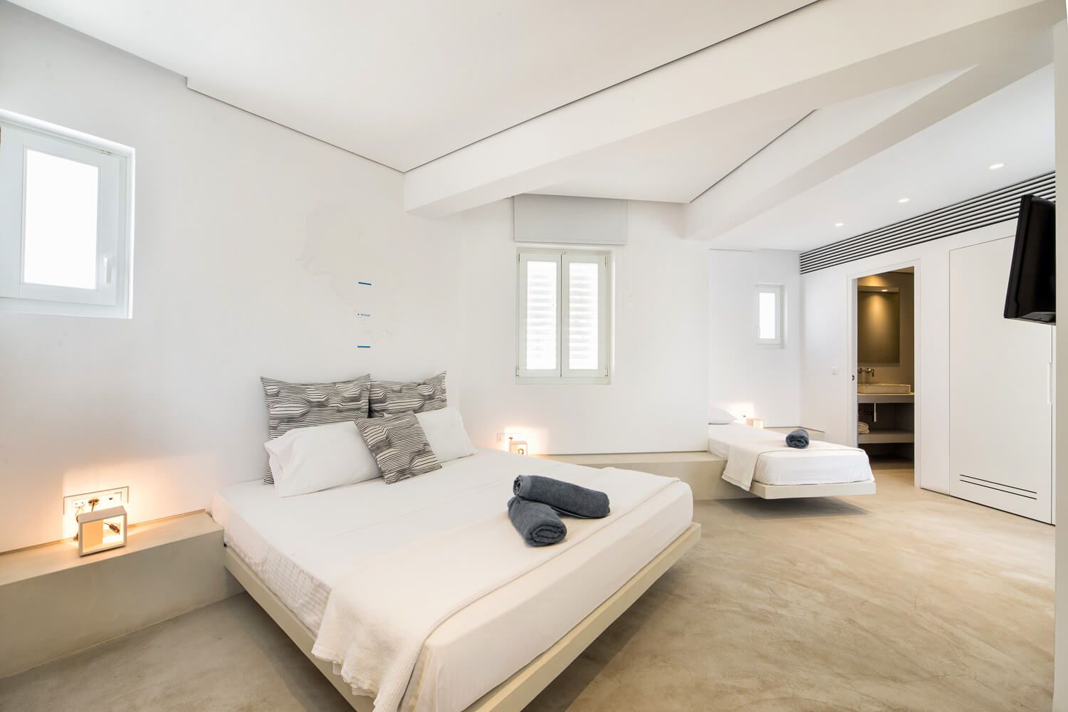 Modern white bedroom interior with vaulted ceiling, natural light, and minimalist decor showcases clean design aesthetic.