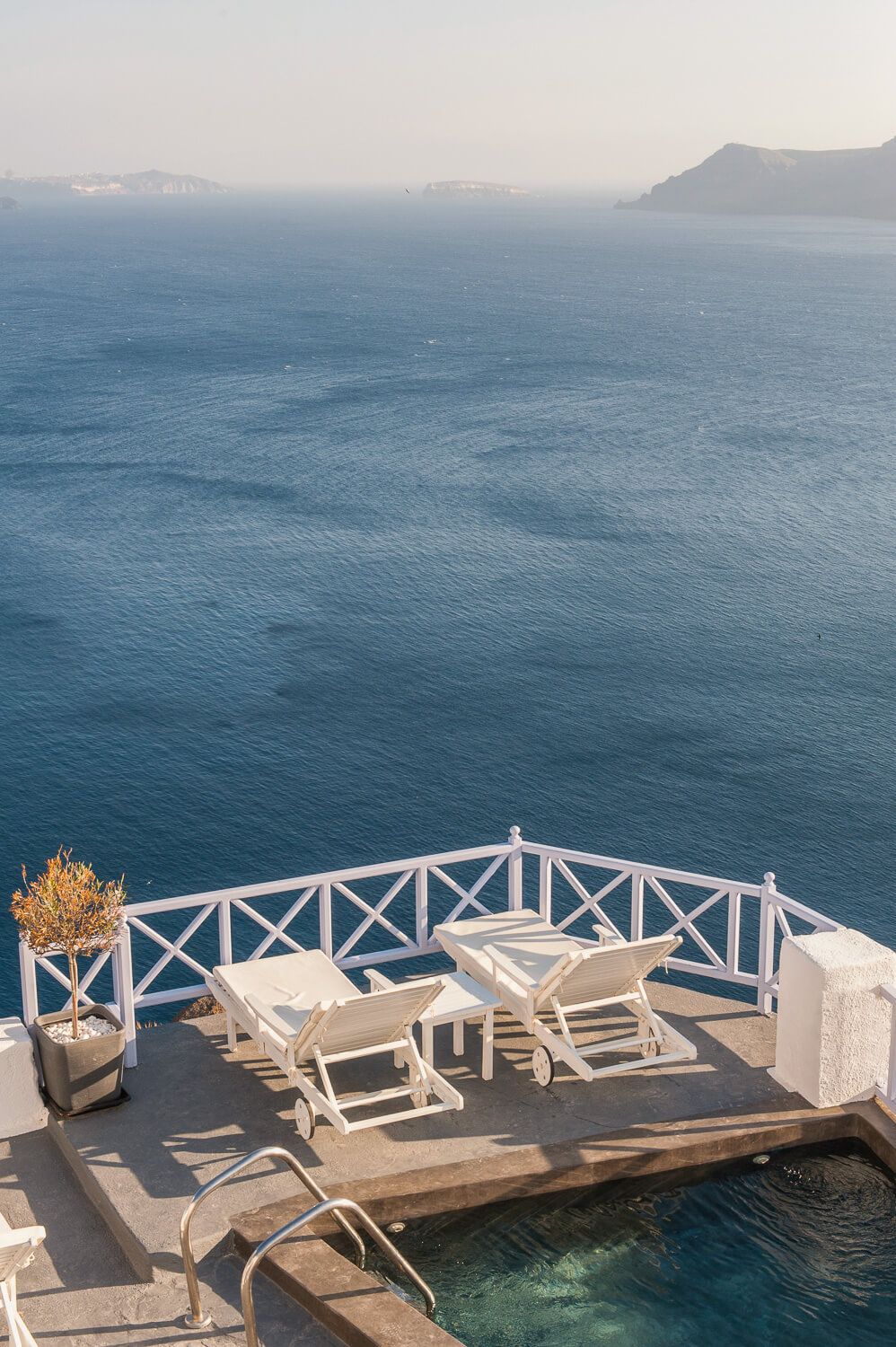 Luxurious white sunbeds on a seaside terrace overlooking the blue Mediterranean waters of Santorini, Greece.