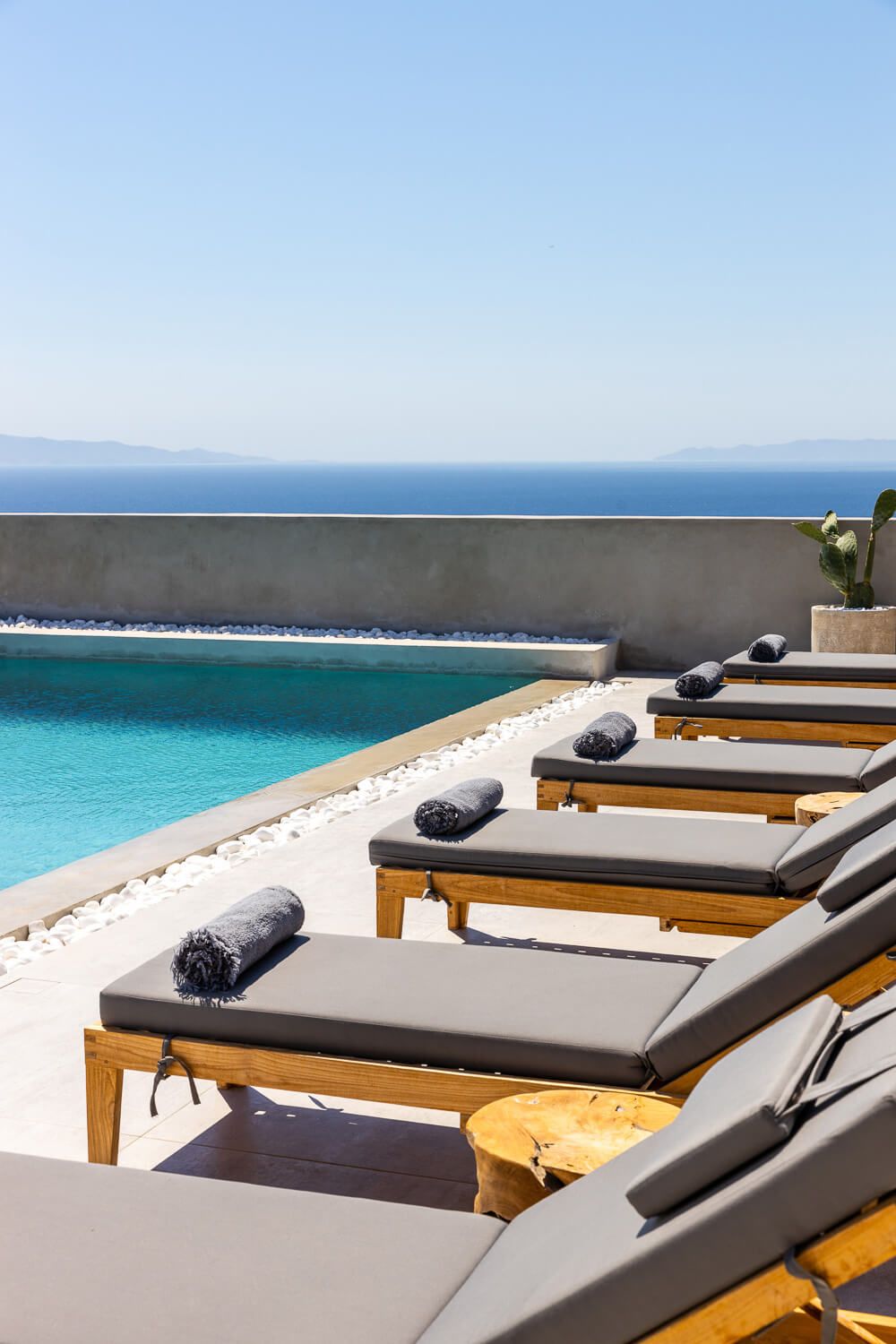 Luxury beach lounge chairs with gray cushions overlooking a pristine turquoise ocean on a sunny day in Greece
