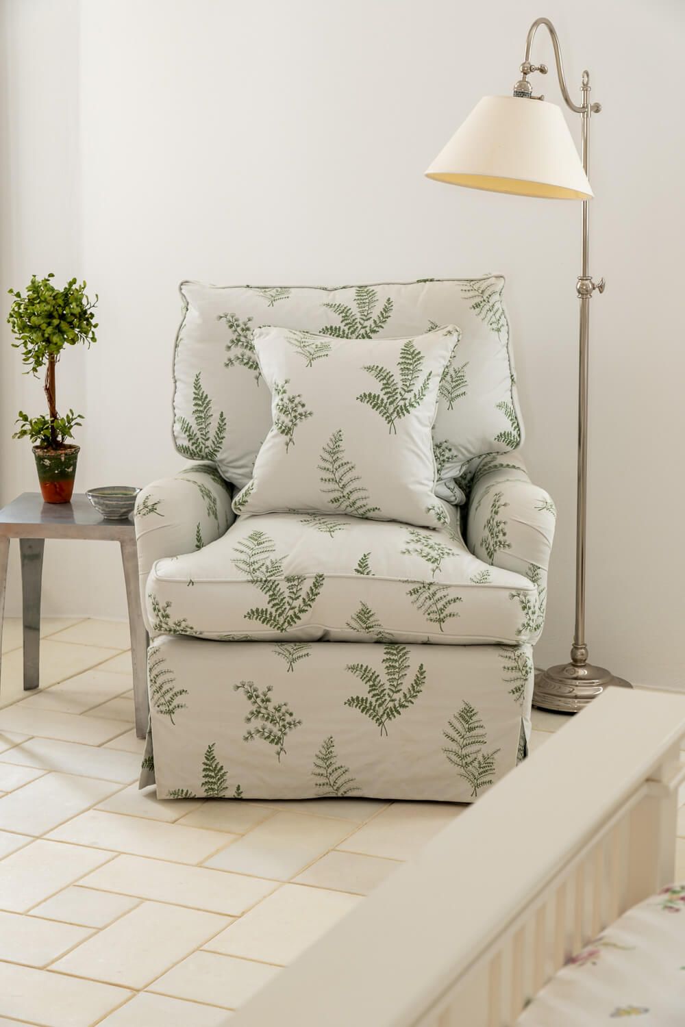 White armchair with botanical fern print pattern cushions styled with floor lamp and potted plant in modern interior in a mansion in Paros