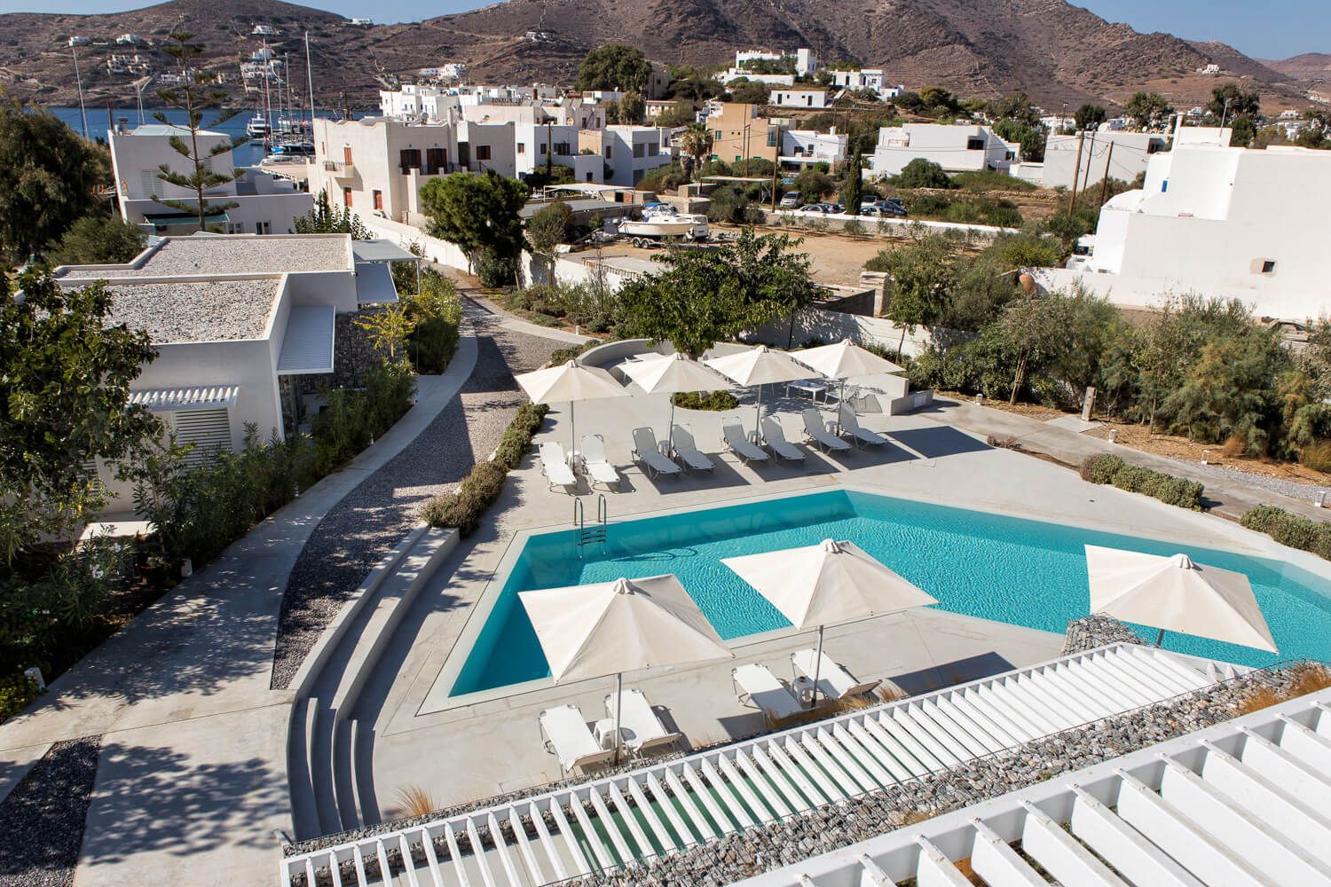 Aerial view of a luxury Mediterranean hotel with white pergola and turquoise swimming pool overlooking coastal mountains.