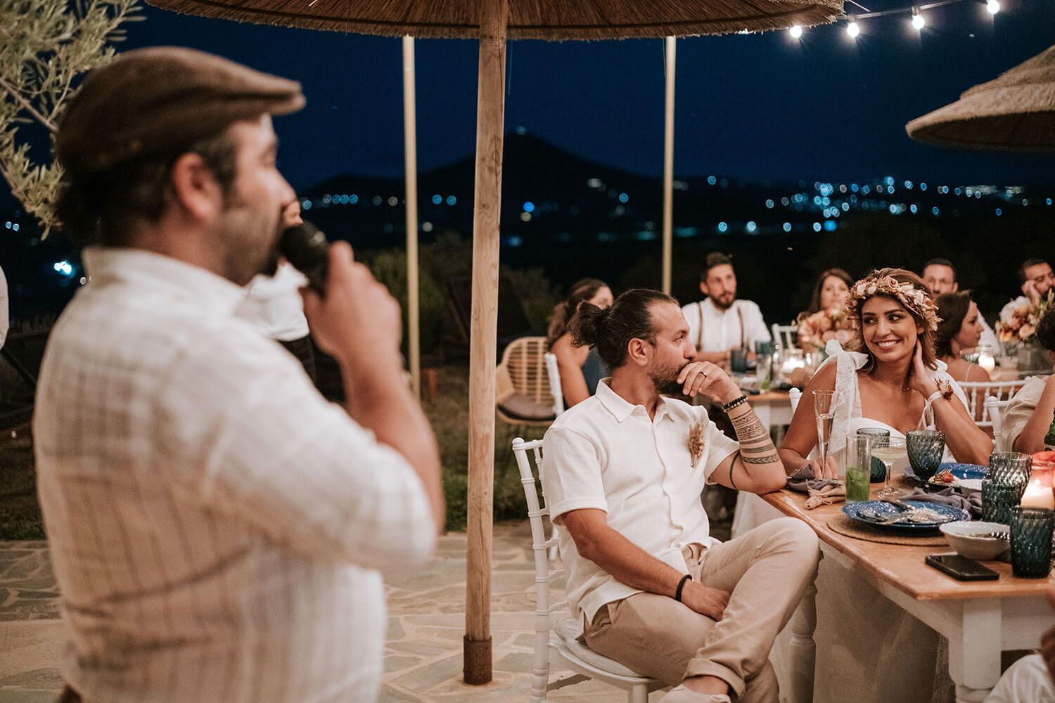 Wedding guests enjoy an outdoor evening reception under string lights at long communal tables.